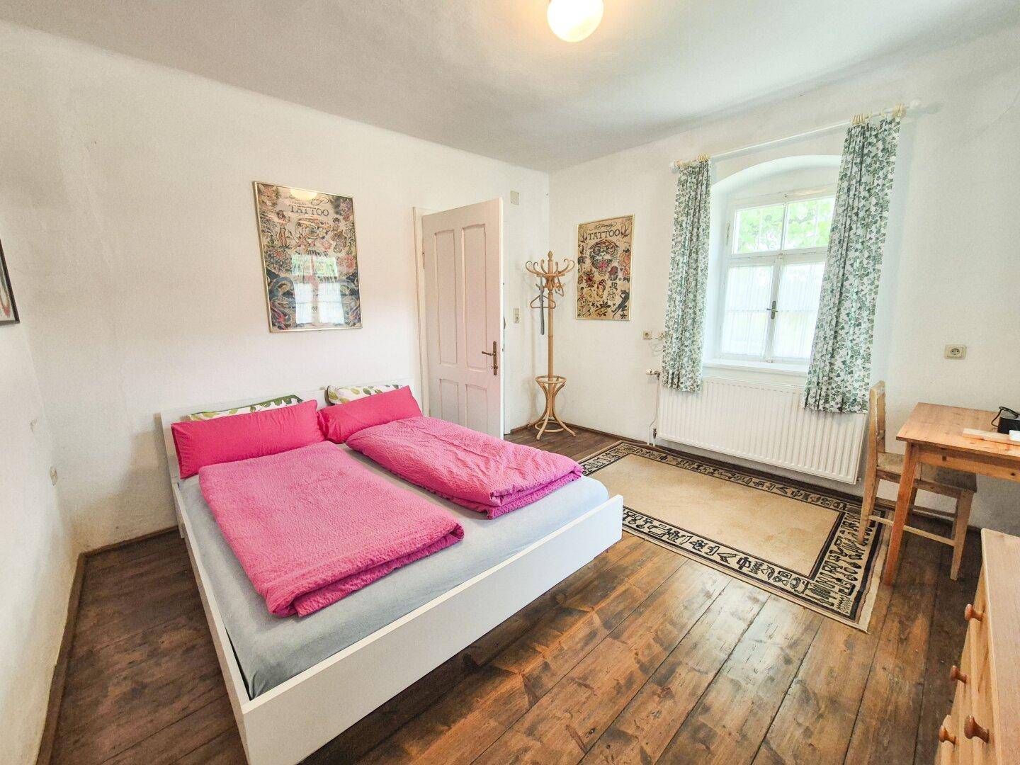 Schlafzimmer mit Holzdielenboden, Doppelbett und traditionellen Vorhängen.