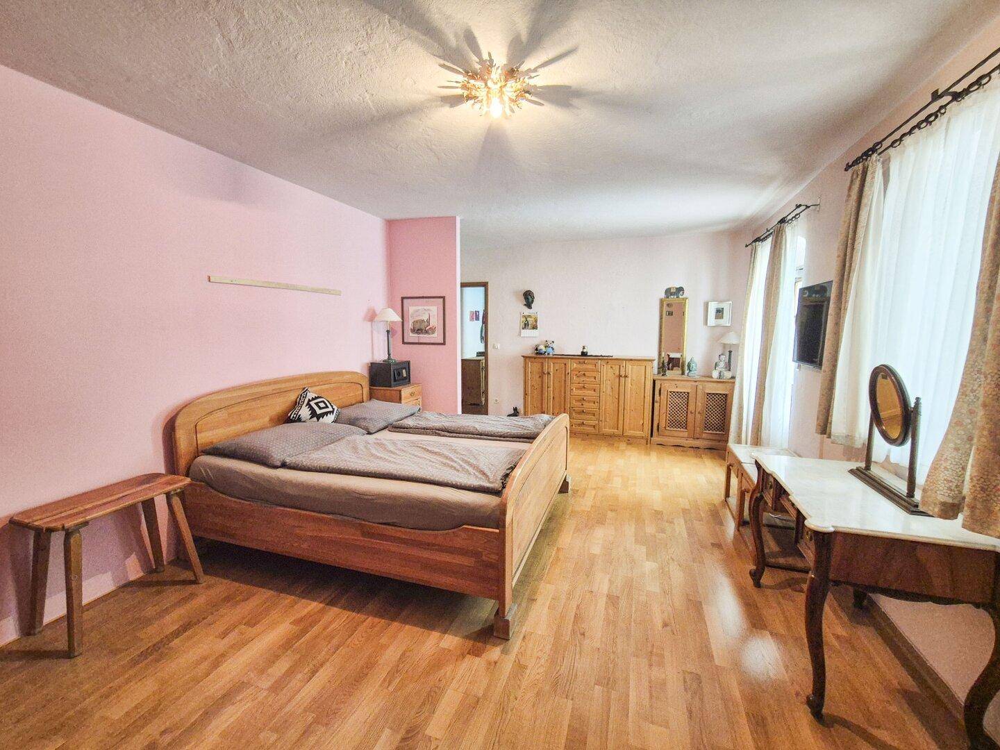 Geräumiges Schlafzimmer mit rosa Wänden, Holzfußboden und traditionellen Möbeln.