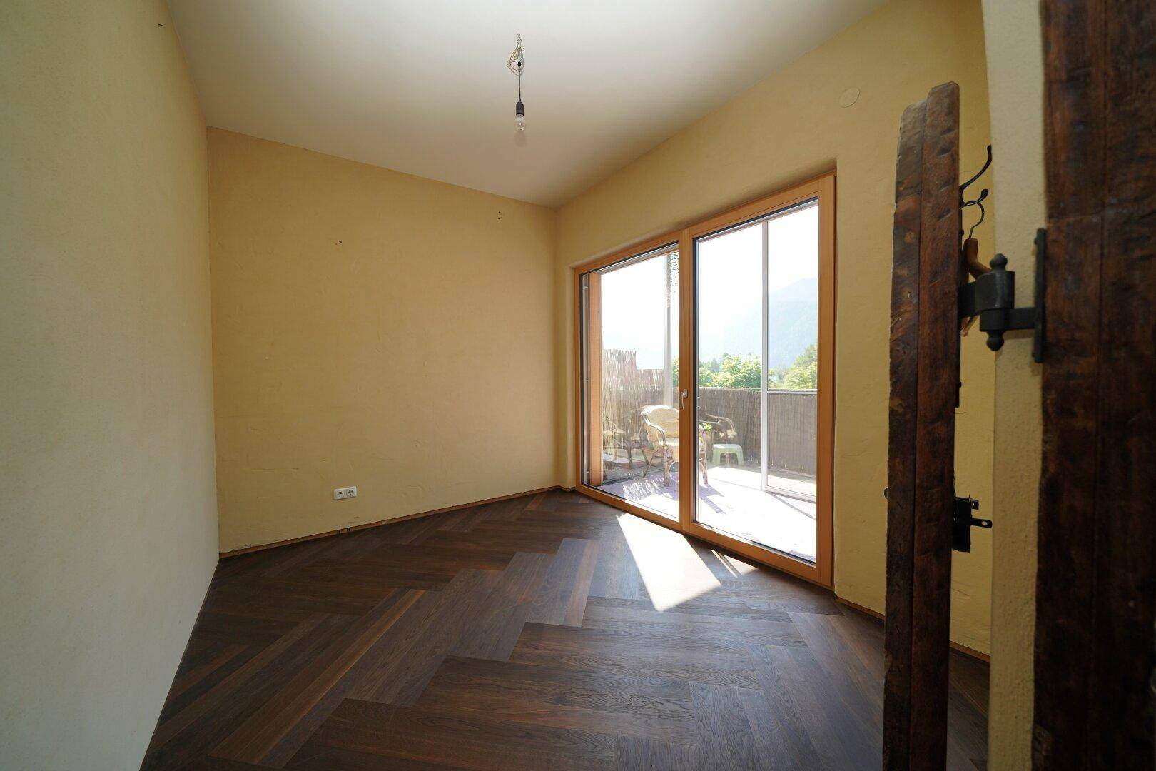 Zimmer mit Fischgrätparkett und großen Schiebetüren, die auf einen Balkon führen.
