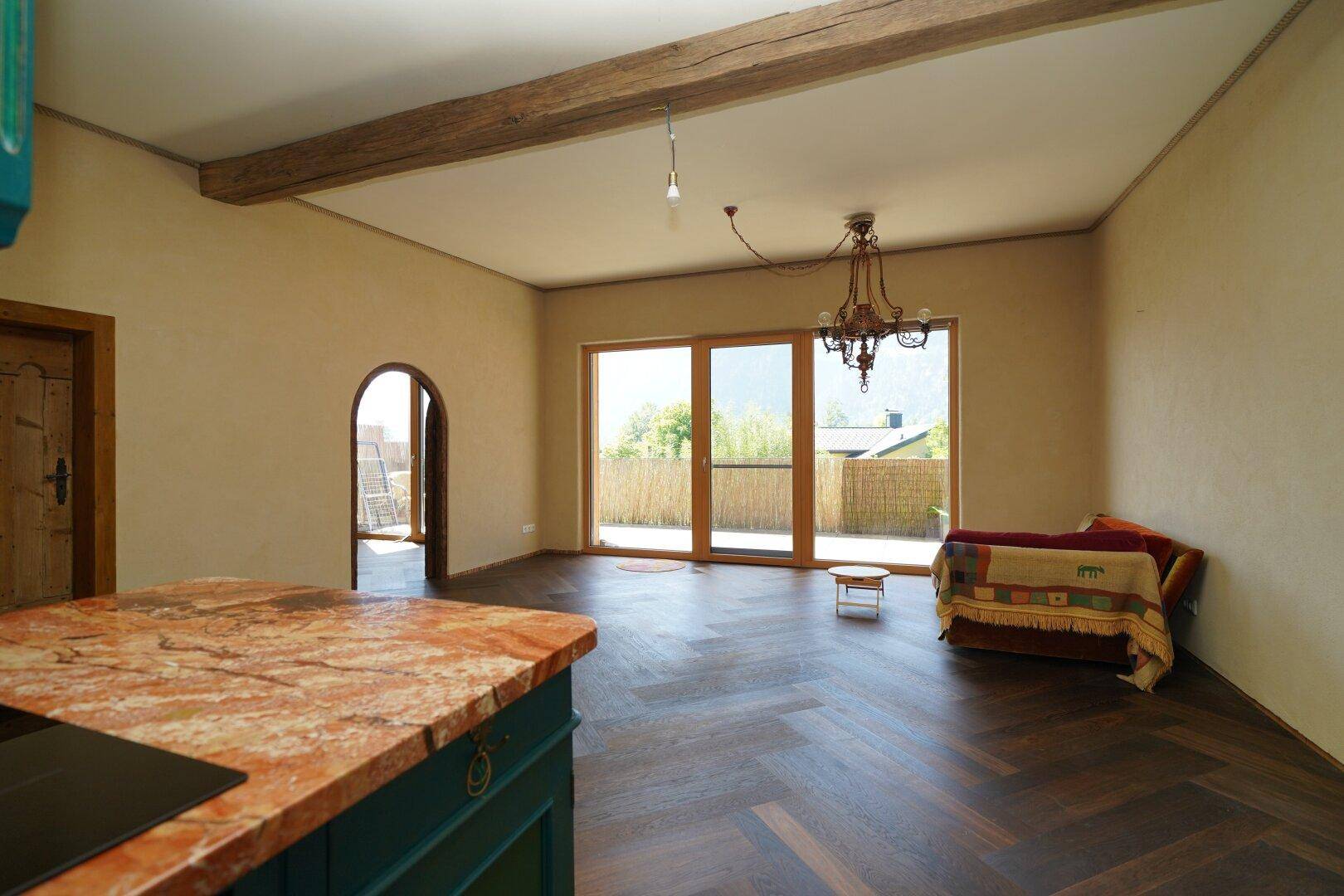 Heller Wohnbereich mit offener Küche, Holzbalken und Zugang zur Terrasse.