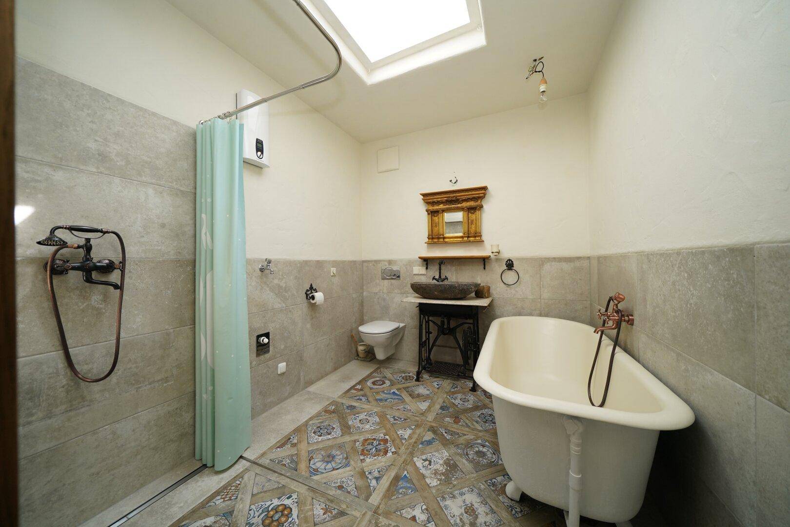 Badezimmer mit freistehender Badewanne, Dusche, gemusterten Fliesen und Dachfenster.