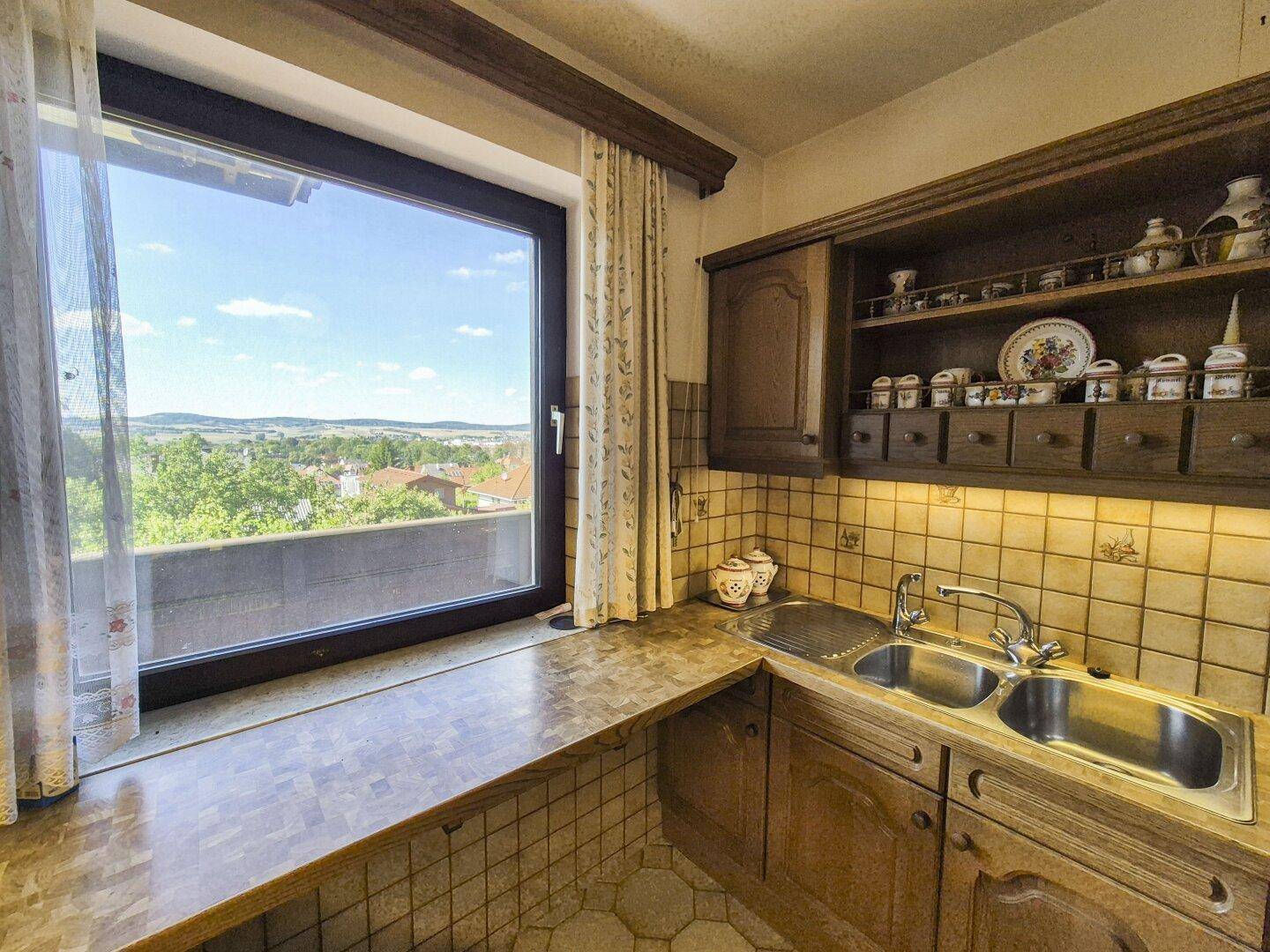Traditionelle Küche mit Holzschränken, Doppelspüle und weitem Ausblick durch das große Fenster.
