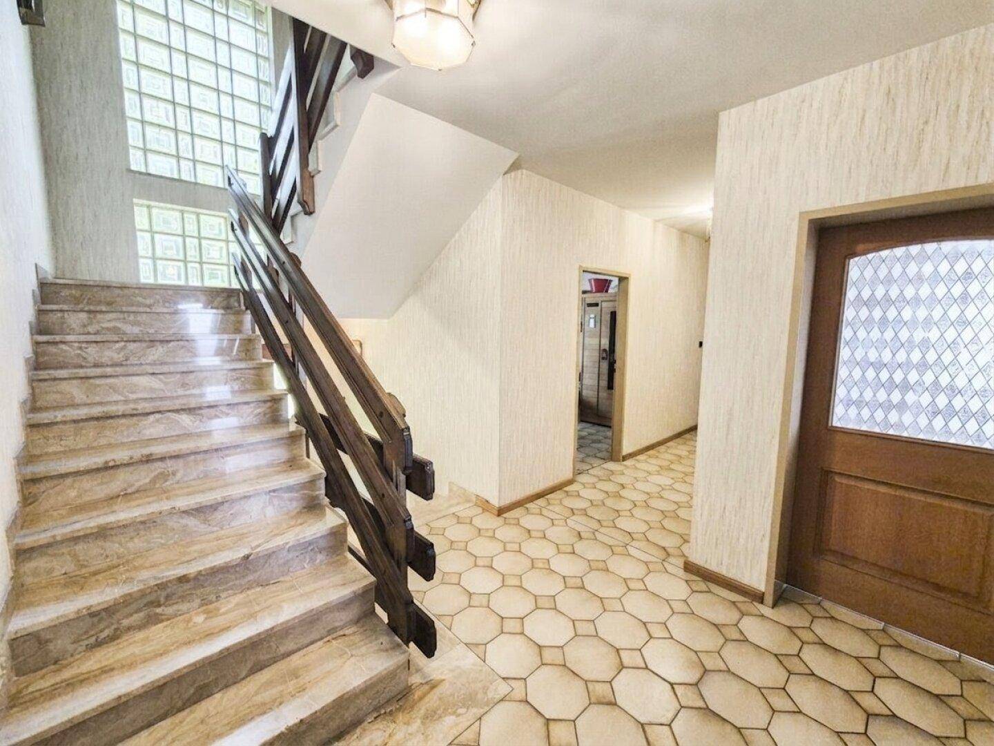 Heller Flur mit Marmortreppe, Holzgeländer und dekorativen Glasbausteinen.