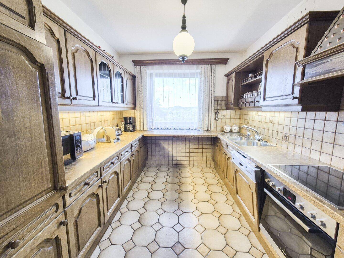 Gemütliche Küche im Landhausstil mit Holzfronten, Fliesenboden und integriertem Backofen.