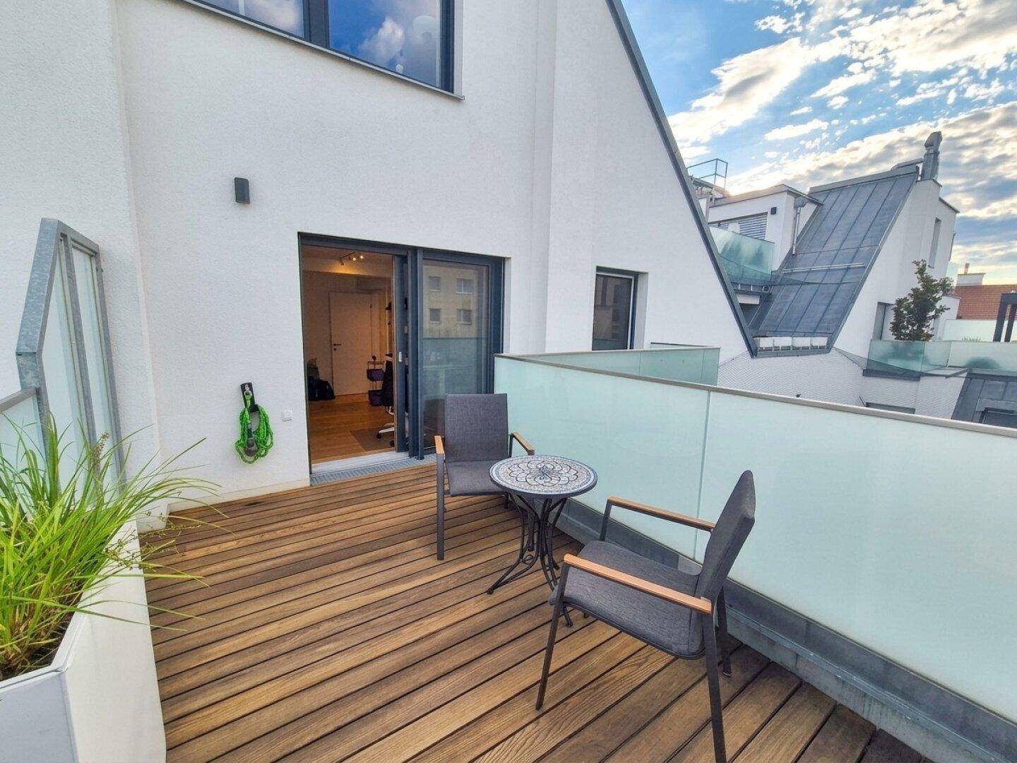 Kleiner Balkon mit Holzboden und Sitzgelegenheiten, umgeben von Pflanzen.