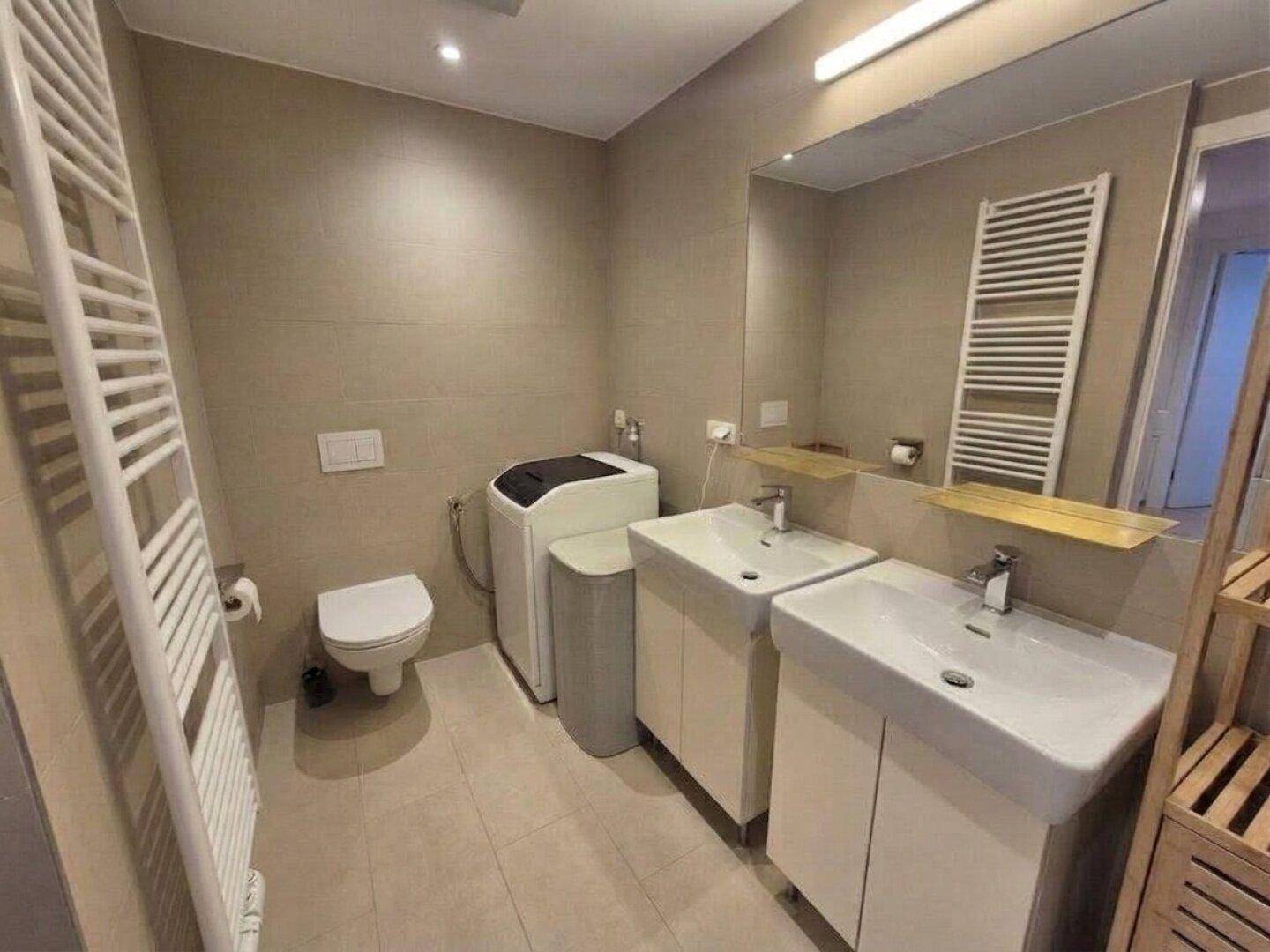 Modernes Badezimmer mit Doppelwaschbecken, WC, Waschmaschine und beheiztem Handtuchhalter.