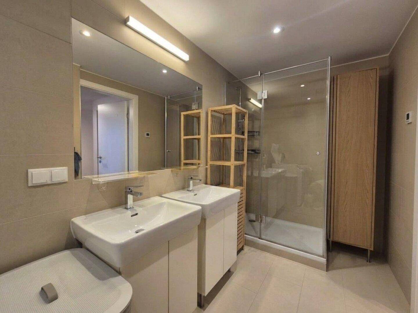 Helles Badezimmer mit Doppelwaschbecken, großer Spiegelfläche und begehbarer Dusche.