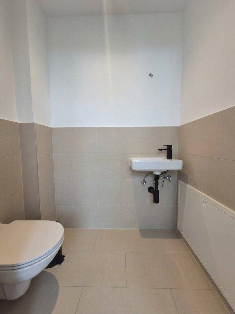 Modernes Gäste-WC mit Wand-WC, kleinem Waschbecken und hellen Fliesen.