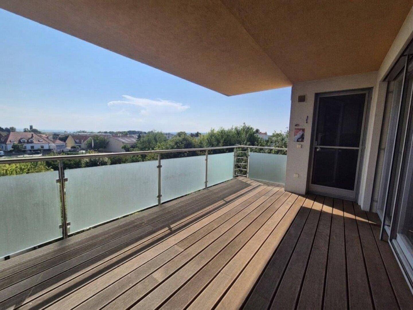 Großer Balkon mit Holzboden und Glasgeländer, bietet weite Aussicht.