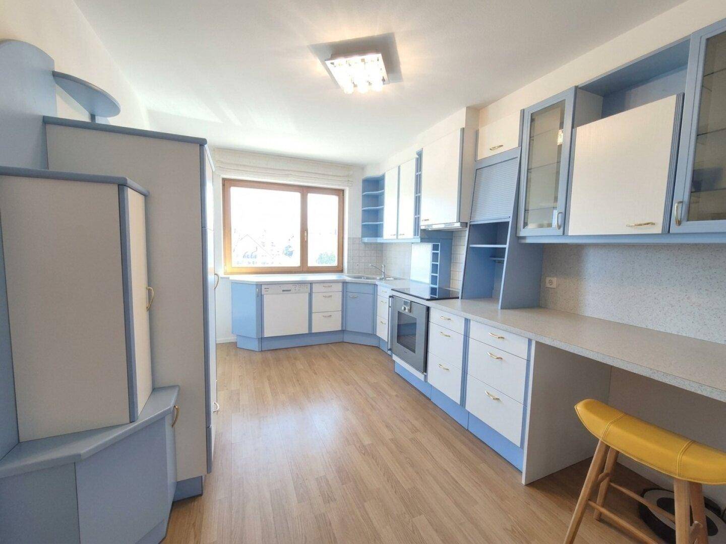 Helle Küche mit blauen und weißen Schränken, ausgestattet mit modernen Geräten und Fenster.
