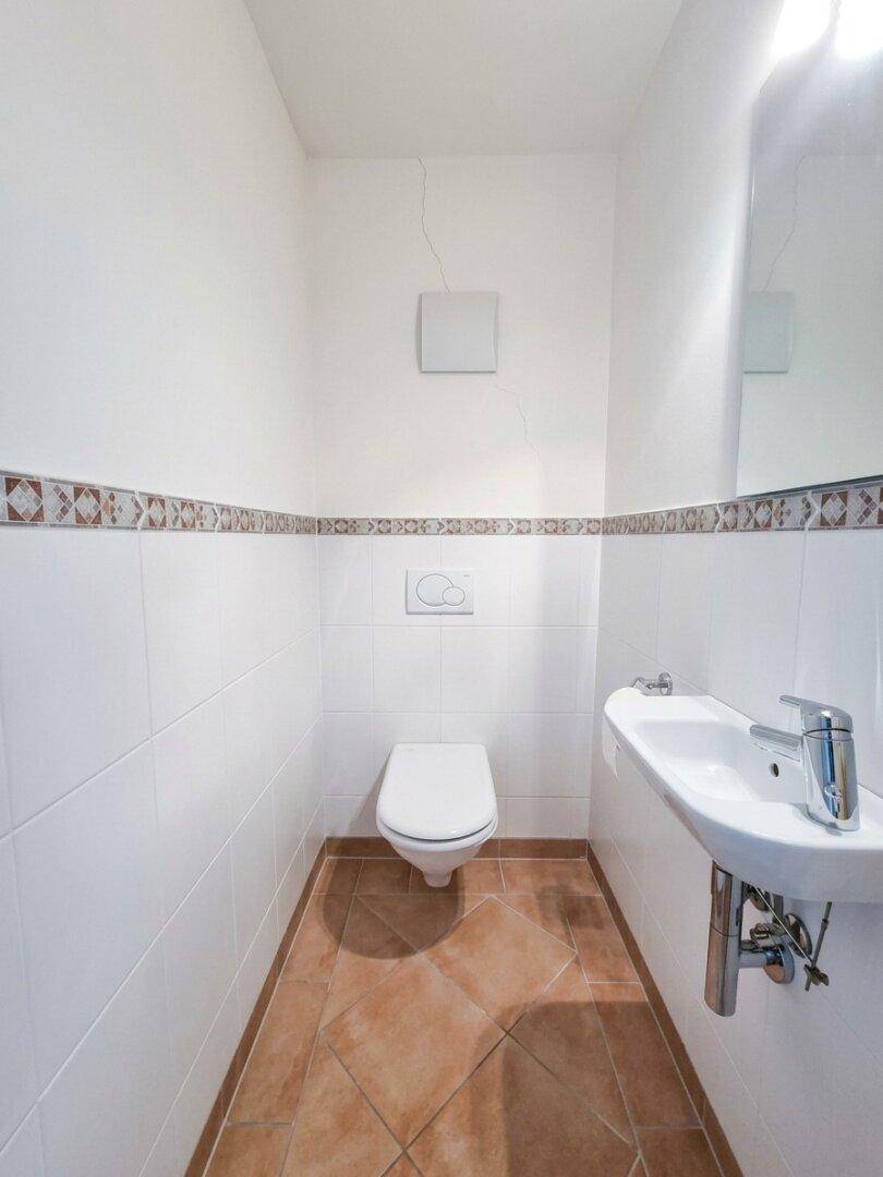 Kleines Gäste-WC mit Wand-WC, Waschbecken und Fliesenboden.