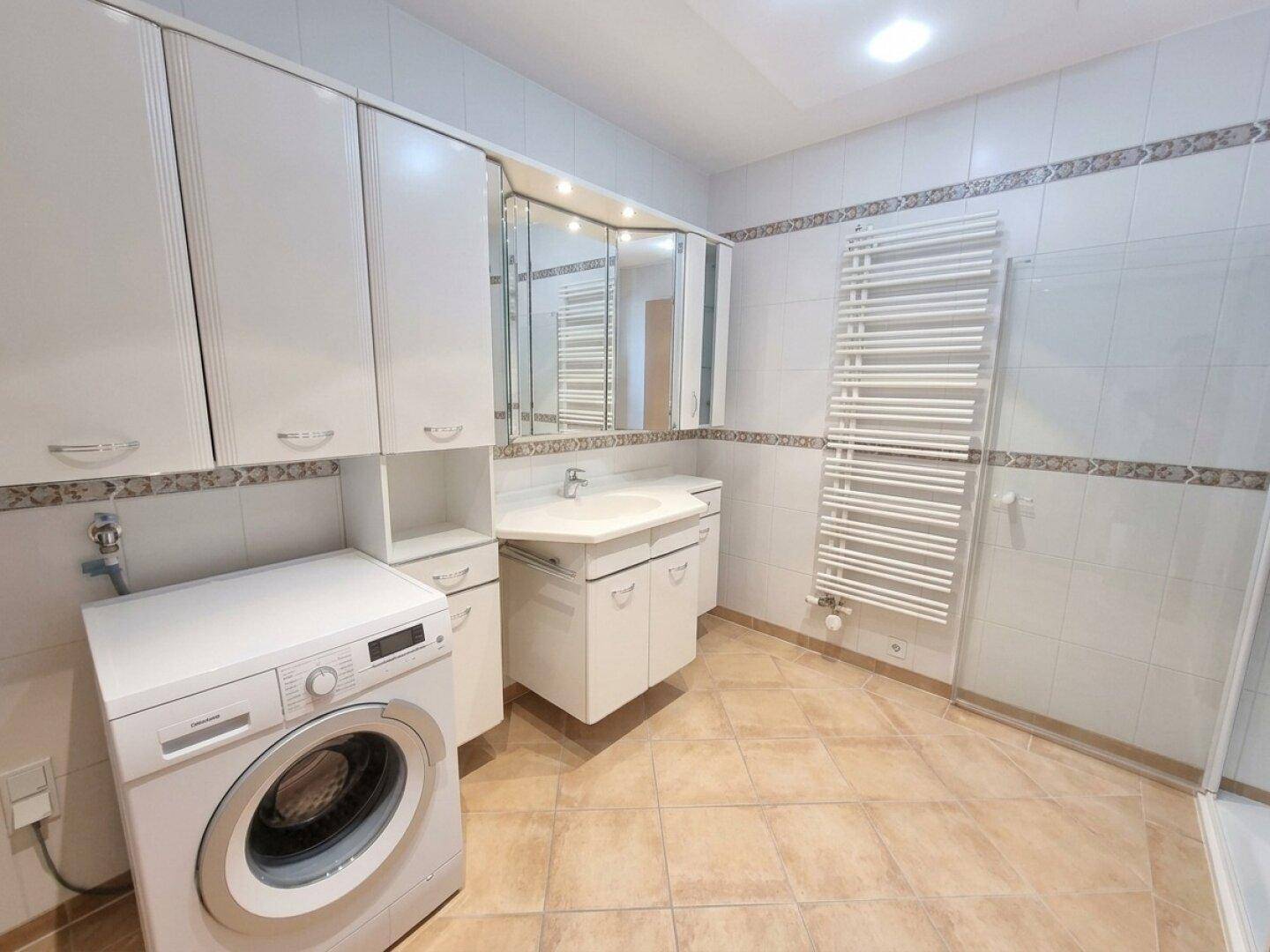 Geräumiges Badezimmer mit Fliesenboden, Waschmaschine und beheiztem Handtuchhalter.