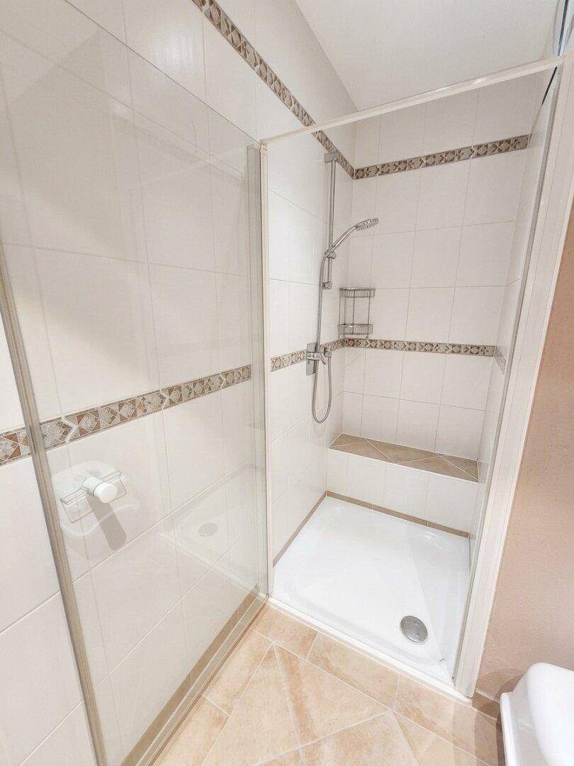 Moderne Duschkabine mit Glaswänden und gefliestem Sitzbereich im Badezimmer.