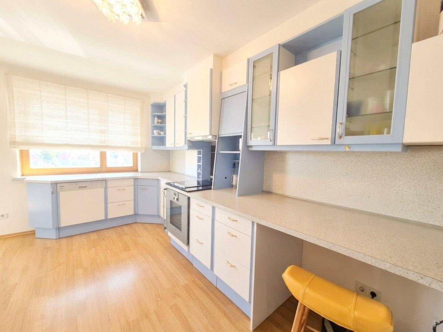 Geräumige Küche mit blauen und weißen Schränken, viel Arbeitsfläche und Fenster.