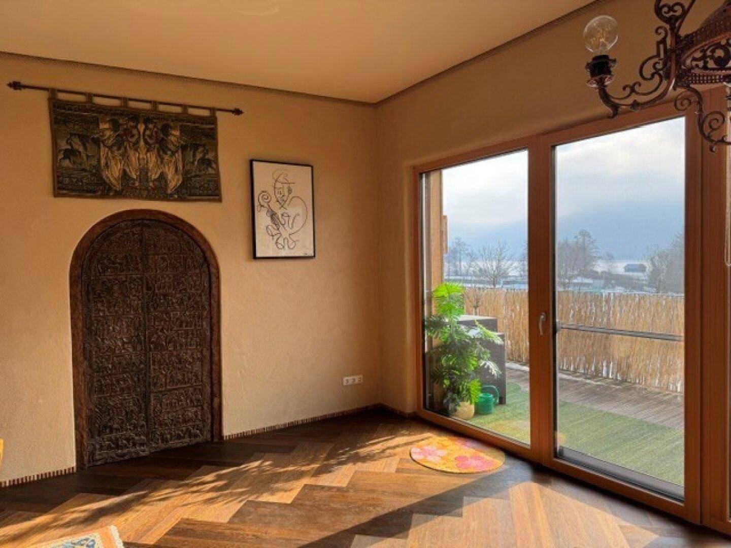 Heller Wohnbereich mit Holzboden, großen Fenstern und Zugang zu einem Balkon mit Blick ins Grüne.