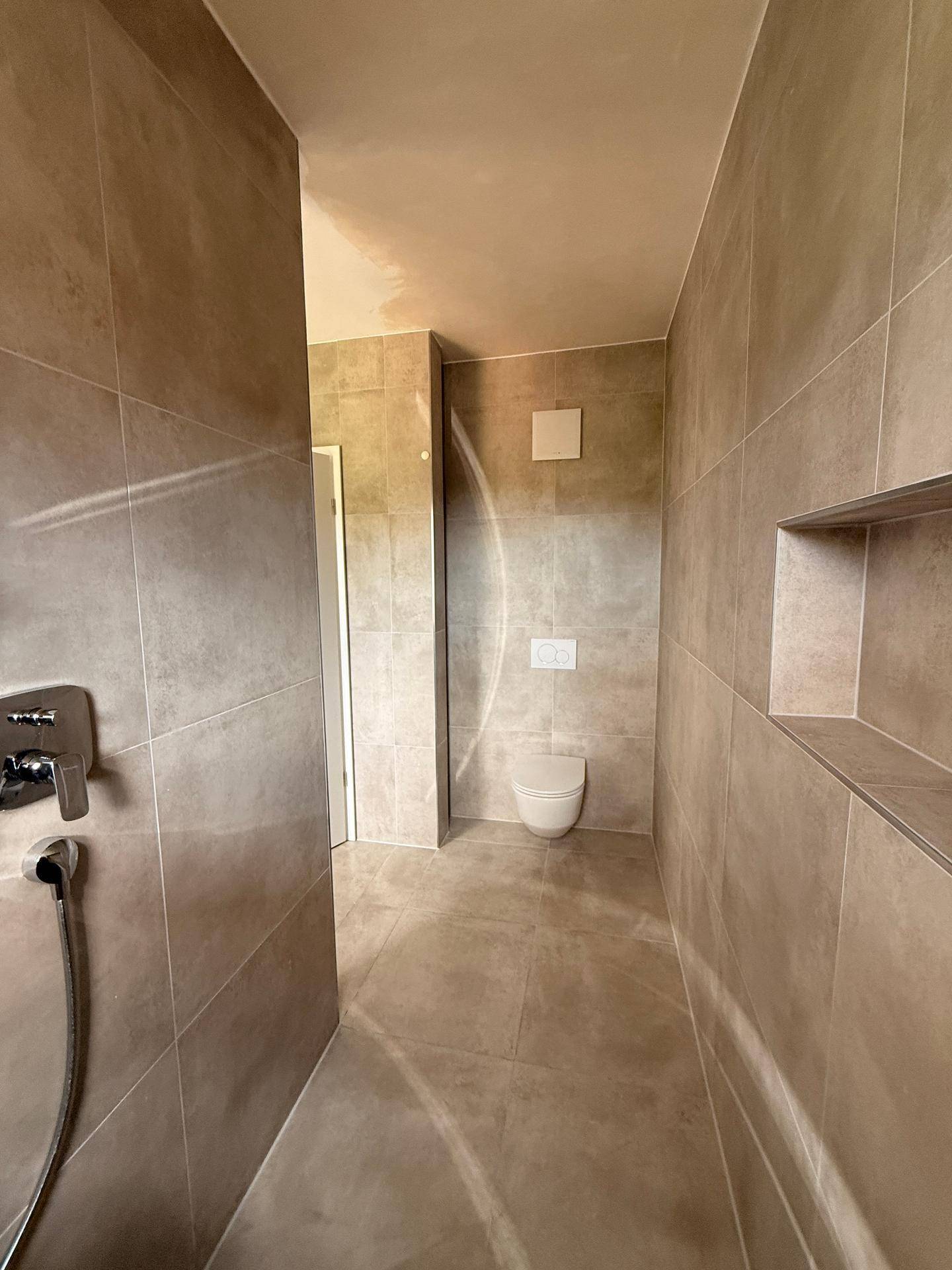 Modernes Badezimmer mit großformatigen grauen Fliesen, Wand-WC und integrierter Duschzone.