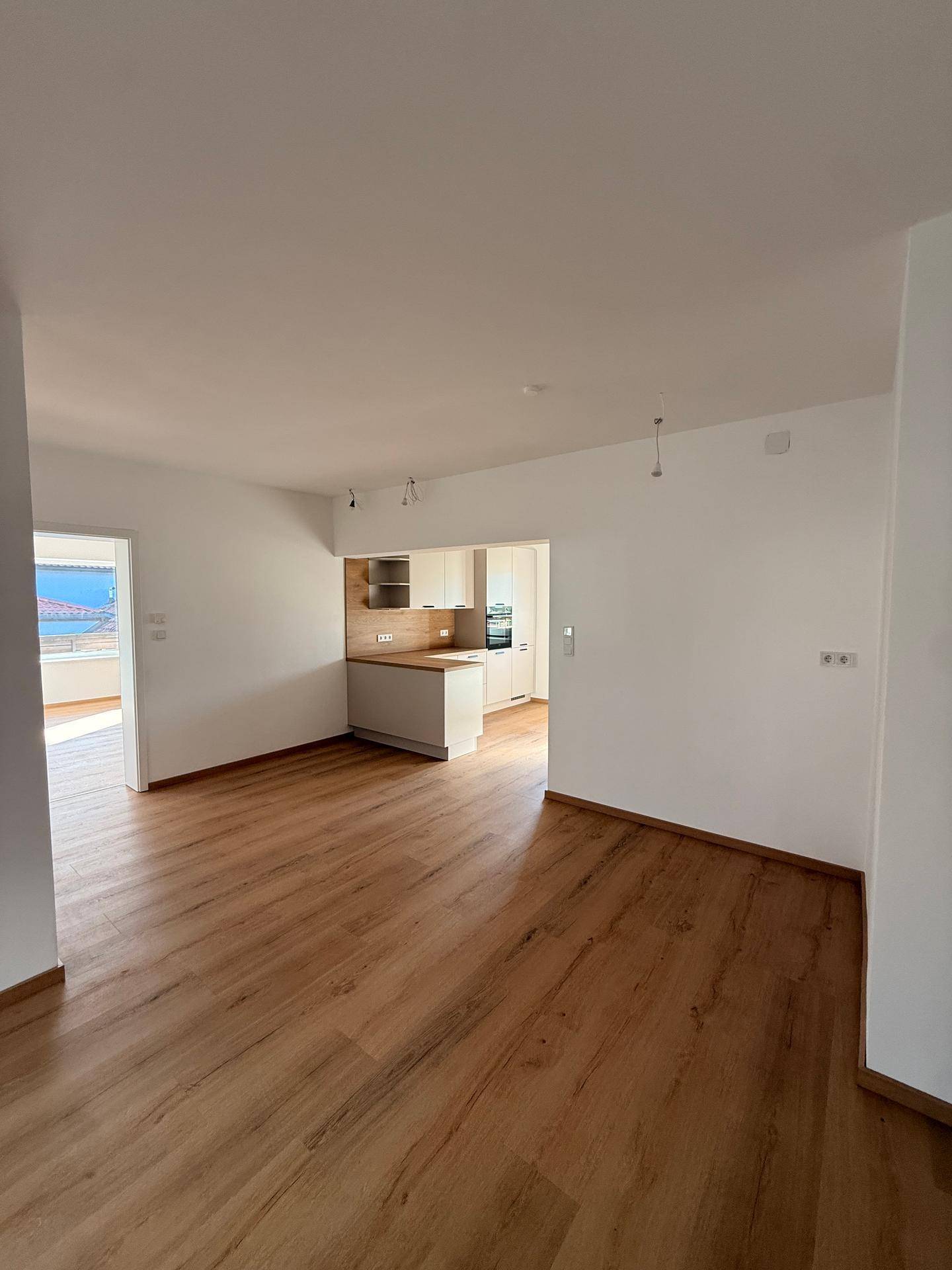 Geräumiger Wohnbereich mit Laminatboden und offenem Übergang zur Küche, ideal für modernes Wohnen.