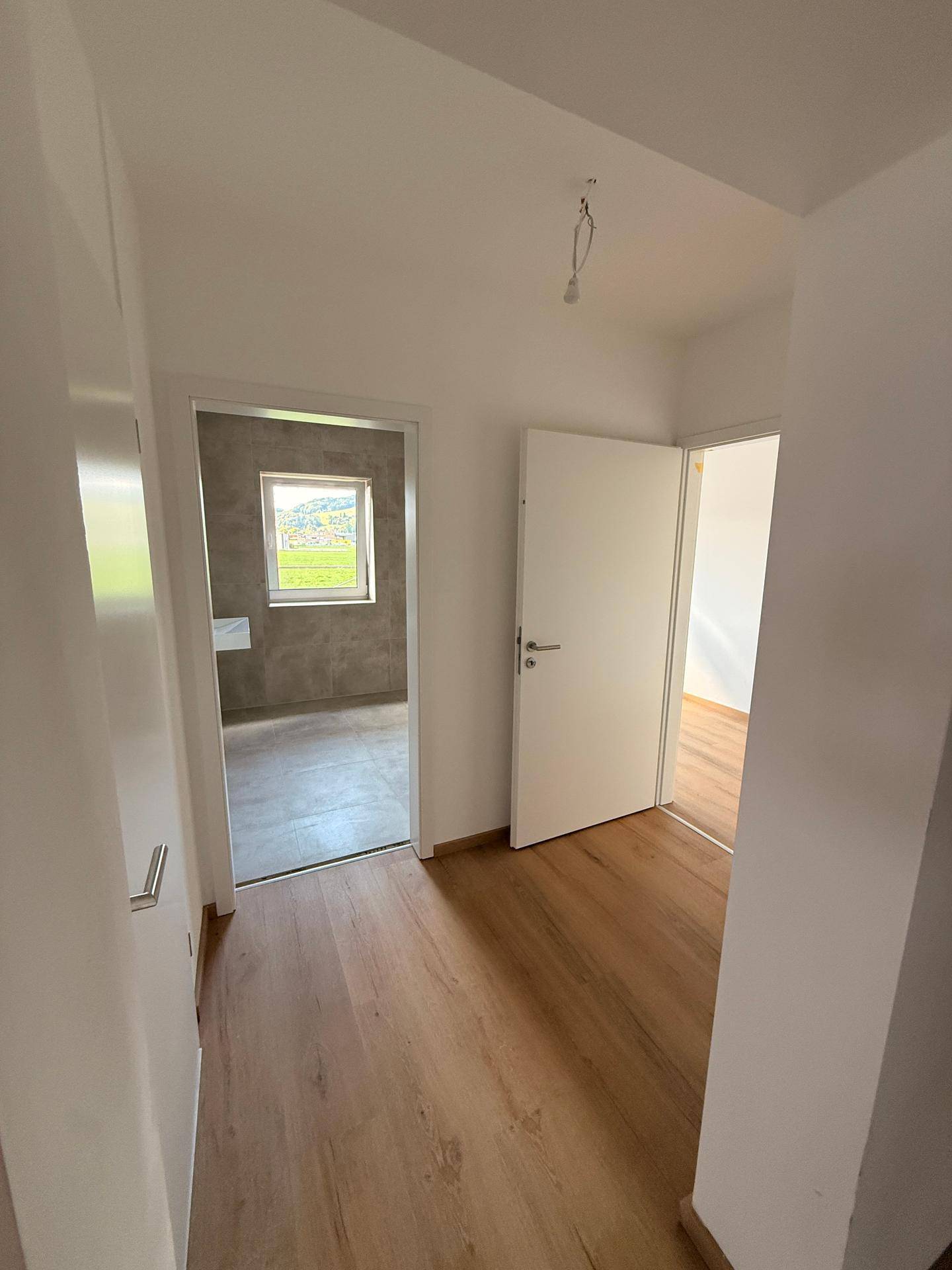 Heller Flur mit Laminatboden, der den Zugang zu einem Badezimmer und weiteren Räumen ermöglicht.
