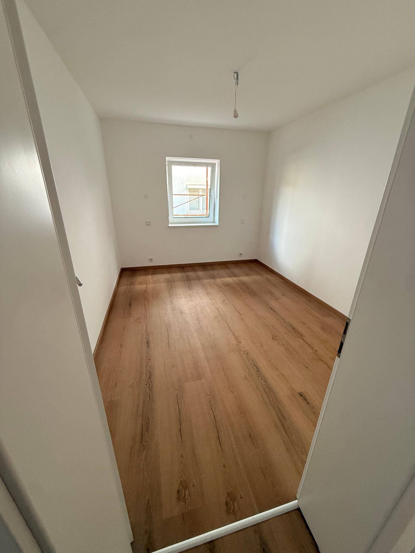 Gemütliches Schlafzimmer mit Laminatboden und einem Fenster, das den Raum hell erscheinen lässt.