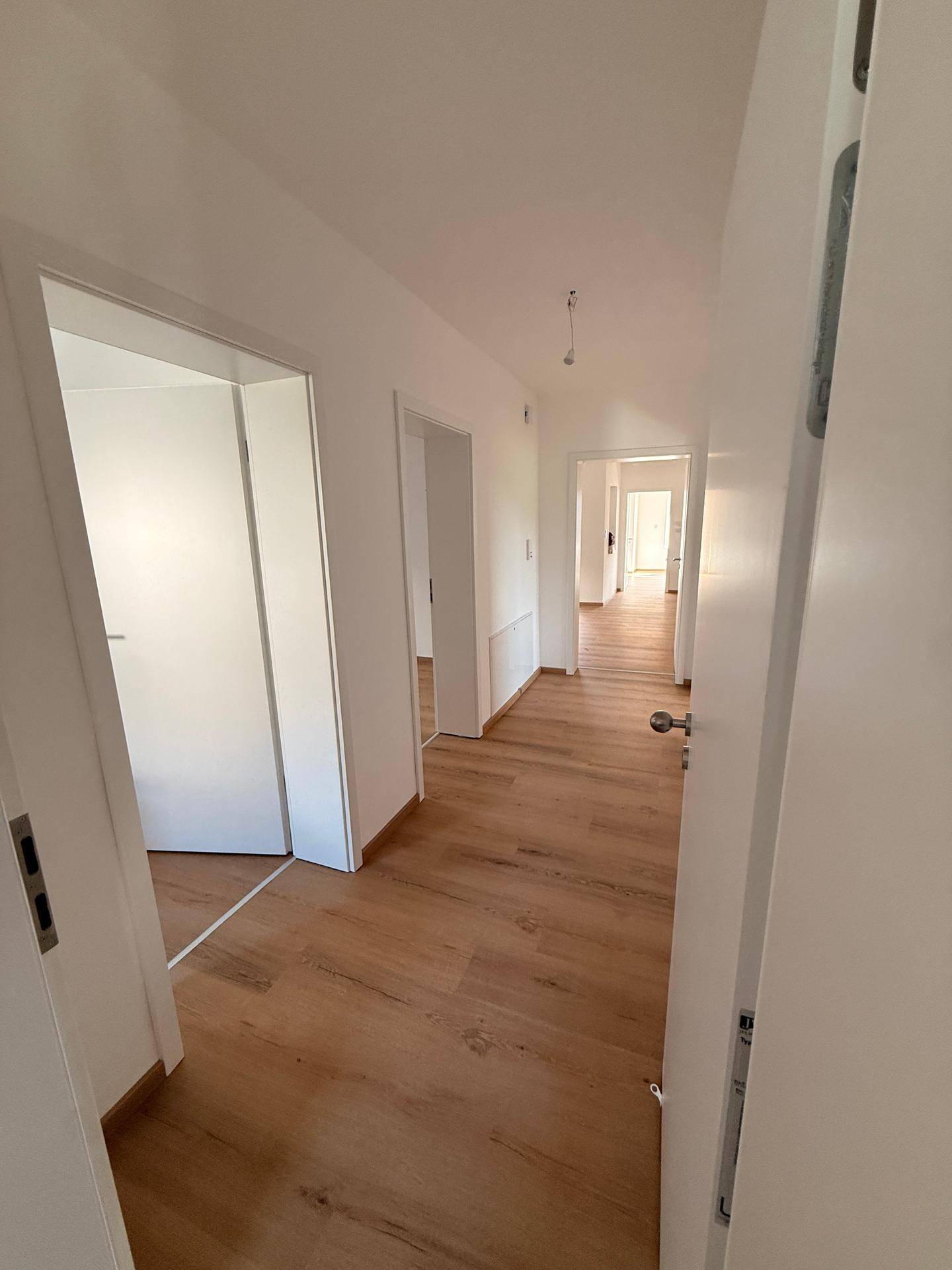 Langer, heller Flur mit Laminatboden, der zu verschiedenen Zimmern führt und gut beleuchtet ist.