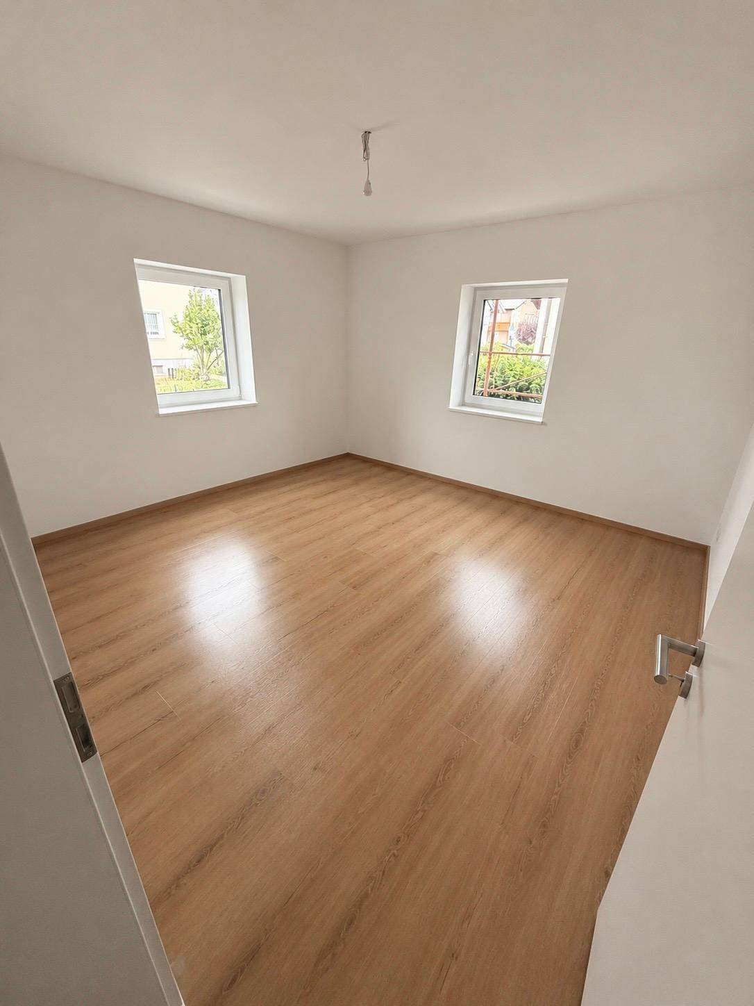 Helles Schlafzimmer mit zwei Fenstern und Laminatboden, bietet eine angenehme Wohnatmosphäre.