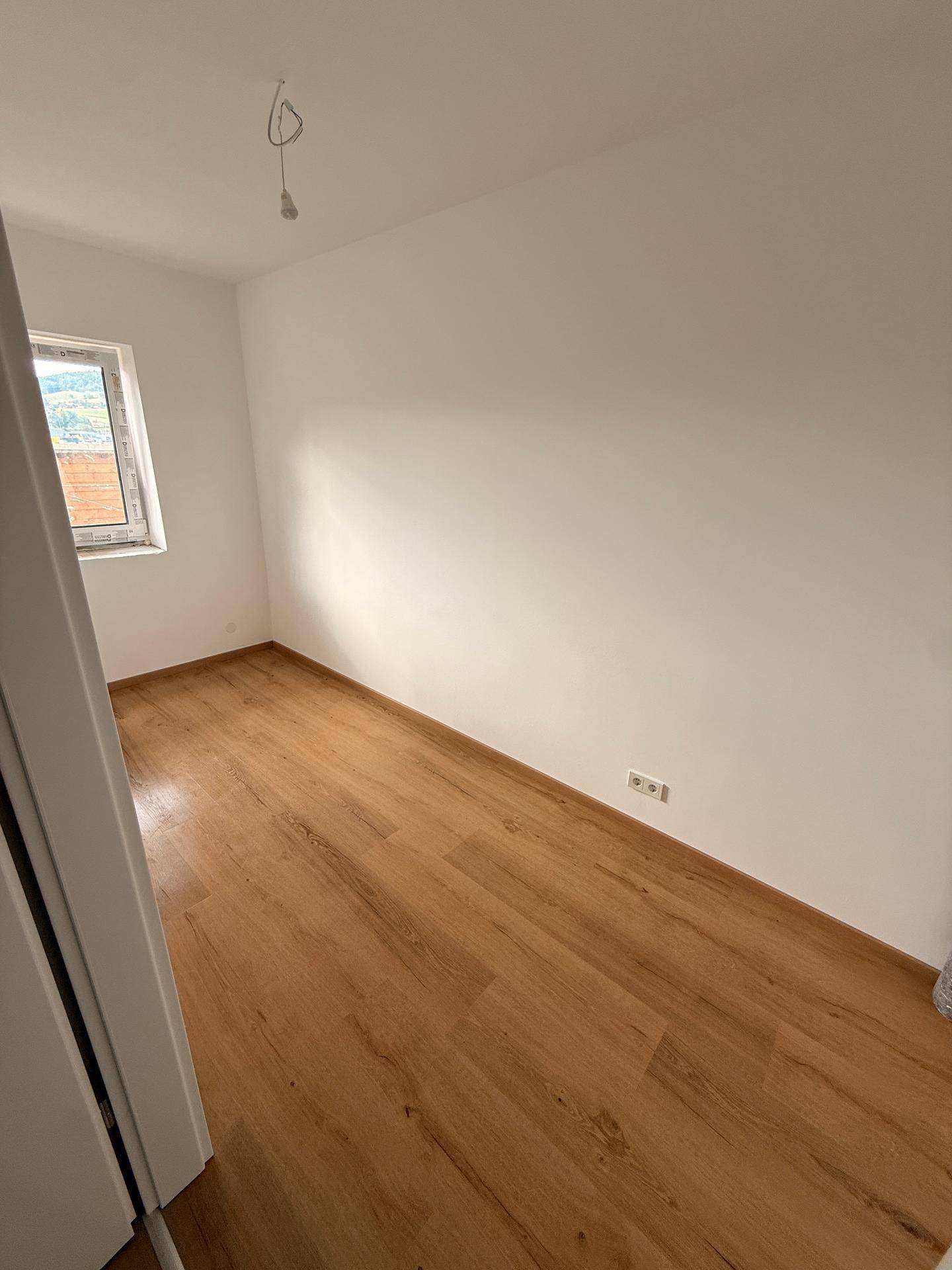 Ruhiges Schlafzimmer mit Laminatboden und Fenster, das viel Tageslicht in den Raum lässt.
