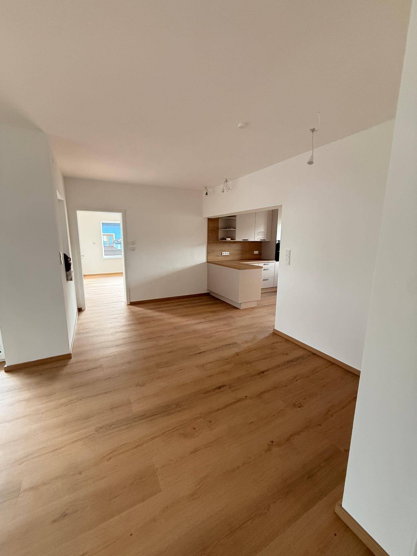Heller Wohnbereich mit durchgehendem Laminatboden, der eine offene Verbindung zur Küche schafft.