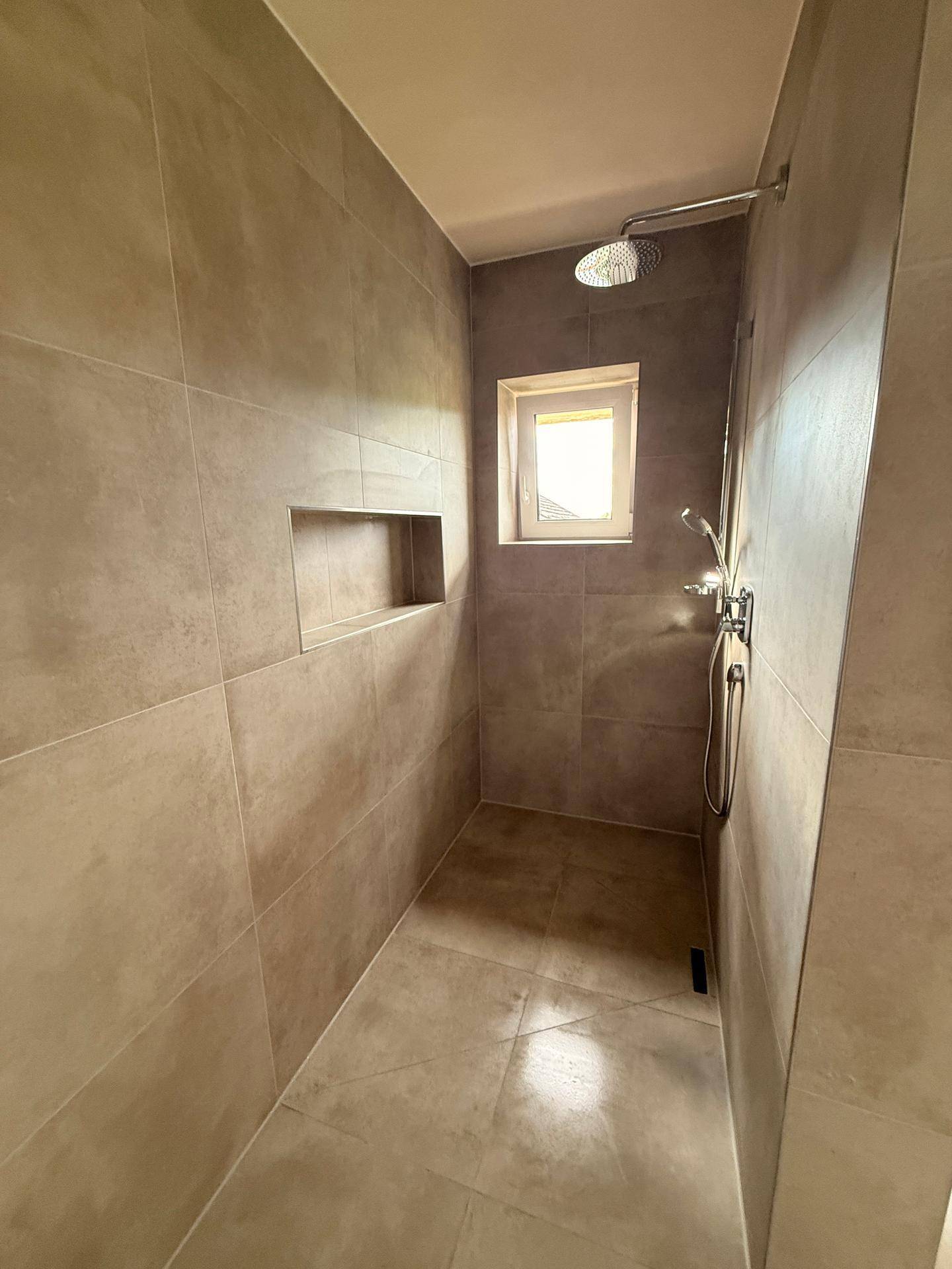 Geräumige, geflieste Dusche mit Regenduschkopf und Fenster, bietet viel natürliches Licht.