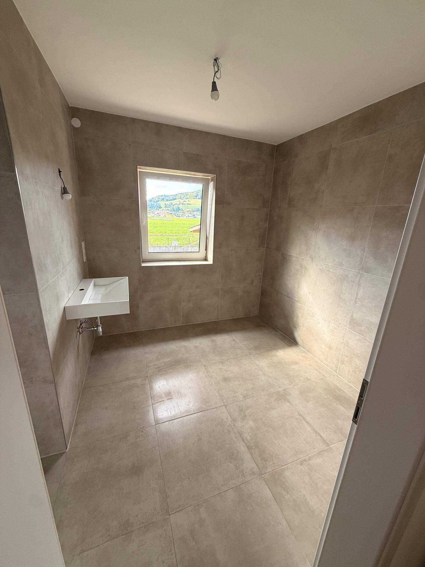 Helles Badezimmer mit großformatigen Fliesen, modernem Waschbecken und Fenster mit Weitblick.