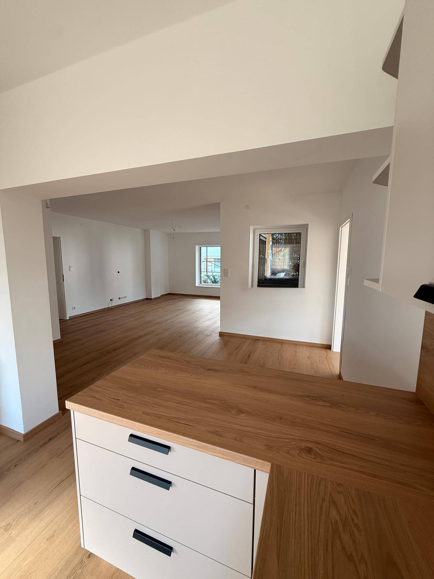 Offener Wohnbereich mit Holzfußboden, der zur modernen Küche übergeht und viel Tageslicht bietet.