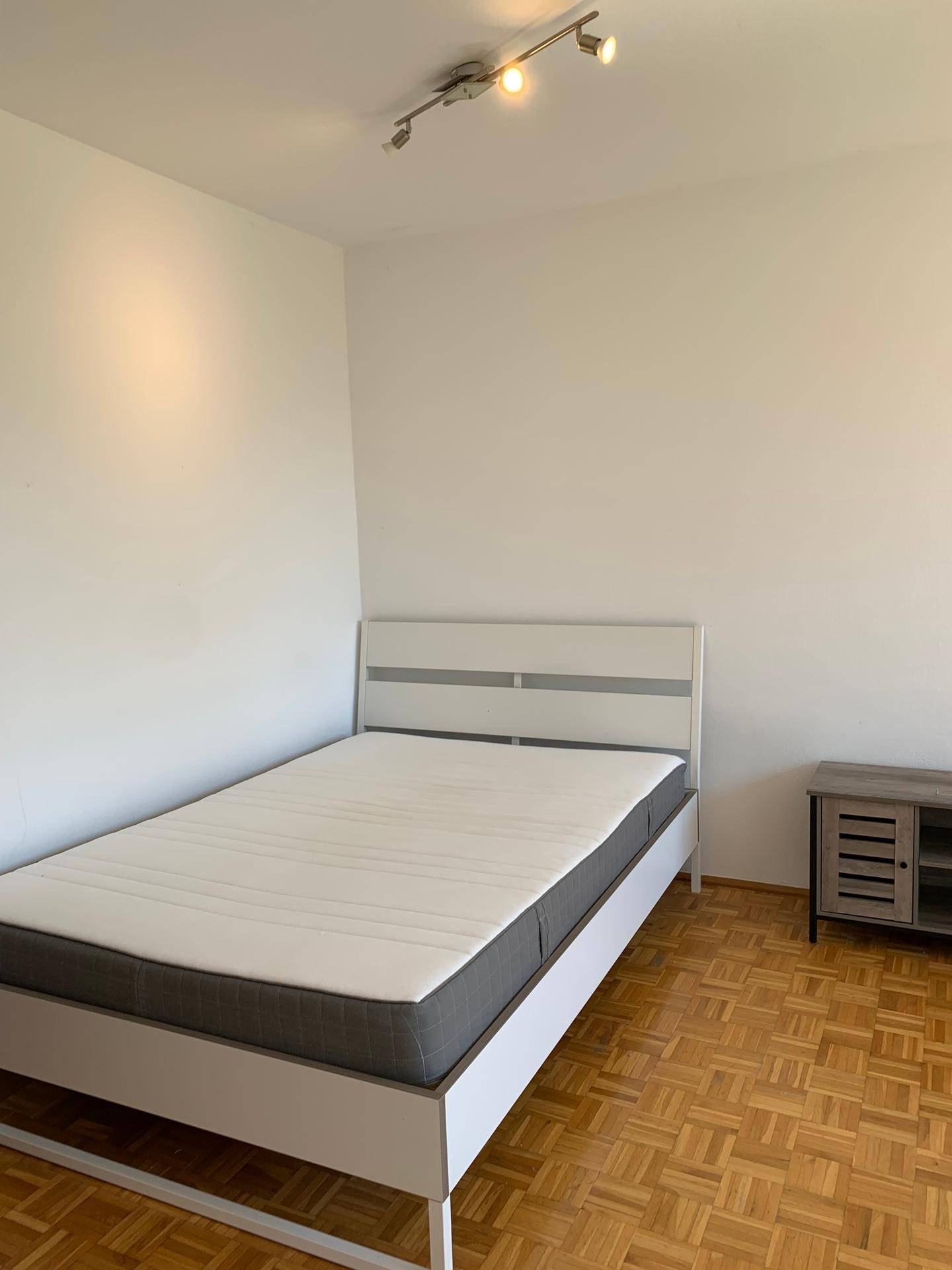 Schlafzimmer mit weißem Bettrahmen und Parkettboden, bereit zur individuellen Einrichtung.
