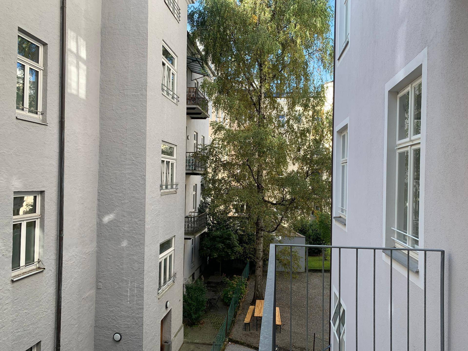 Blick vom Balkon in einen grünen Innenhof mit Bäumen und Sitzgelegenheiten zwischen den Gebäuden.