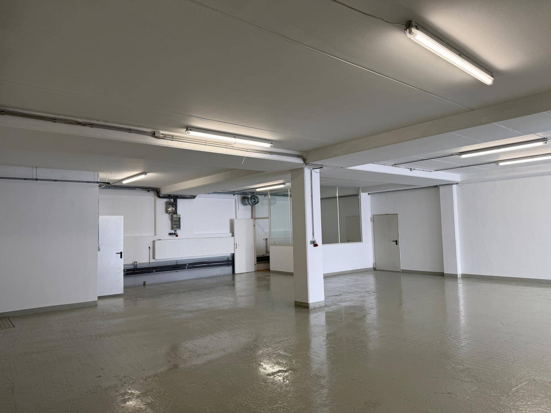 Geräumiger, sauberer Gewerberaum mit Säulen, hellgrauem Boden und sichtbaren Installationen an der Decke.