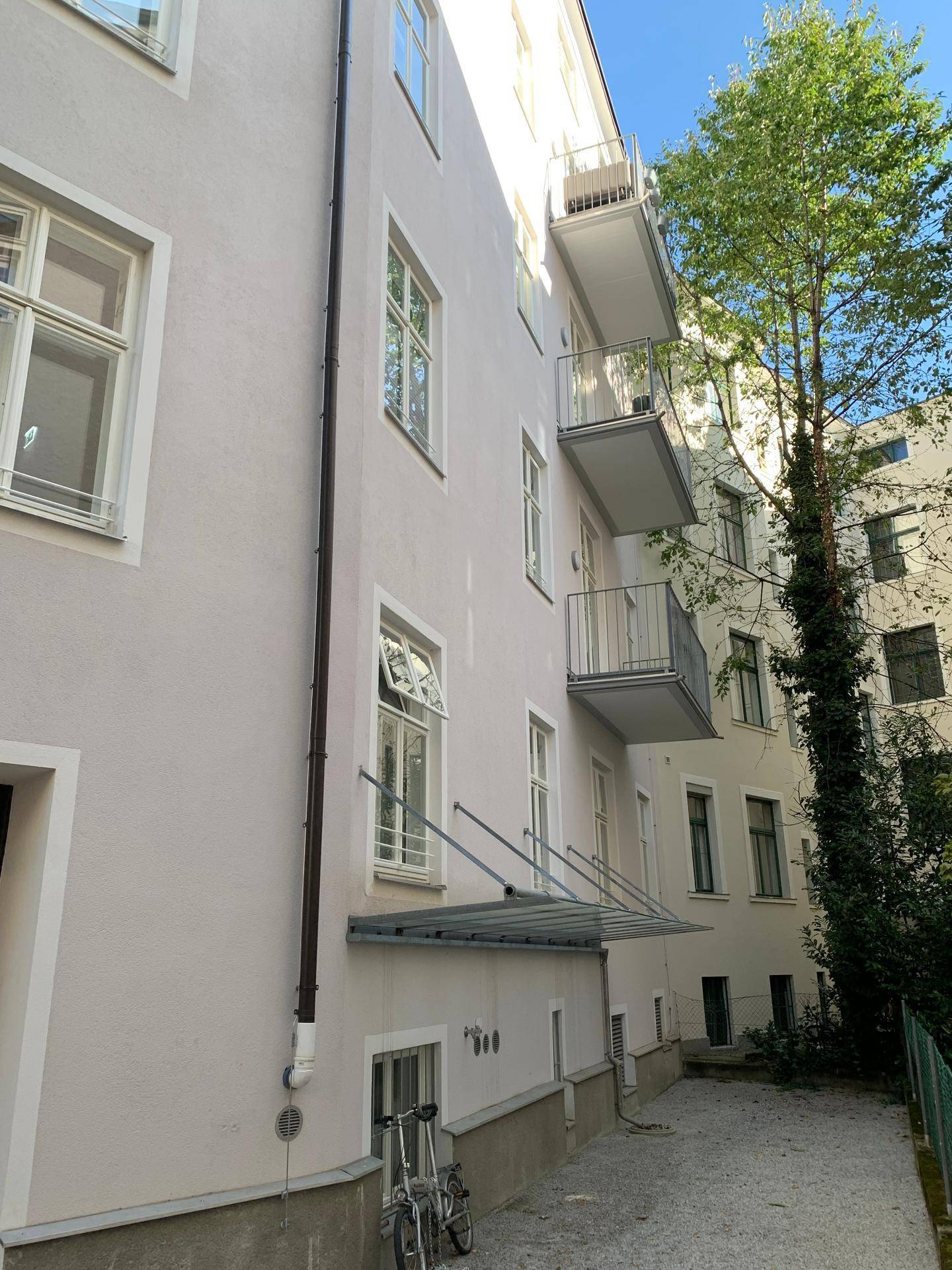Seitenansicht des Gebäudes mit mehreren Balkonen und einem schmalen Zugang zum Hinterhof.
