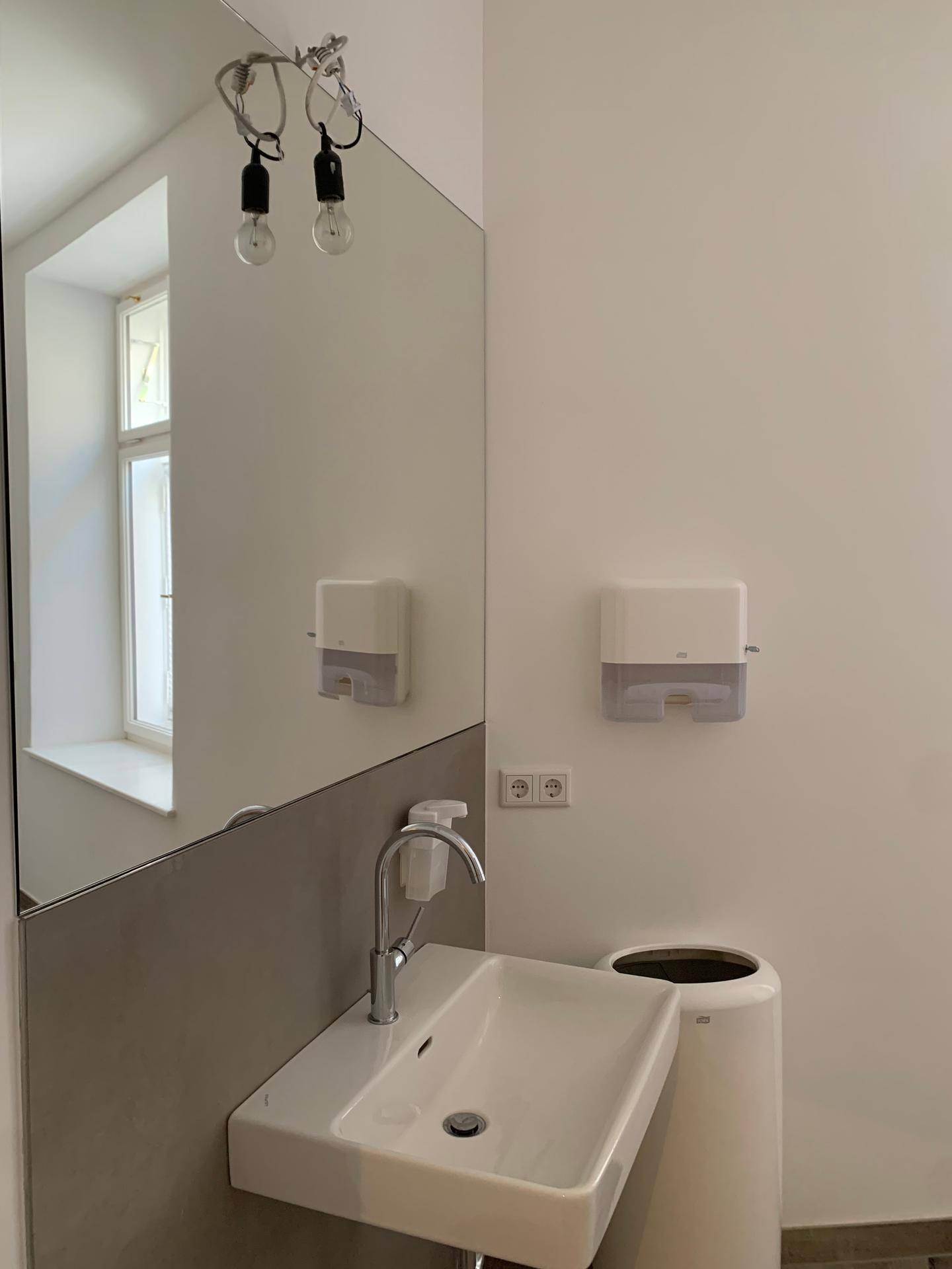 Modernes Badezimmer mit Waschbecken, großem Spiegel und Fenster für Tageslicht.