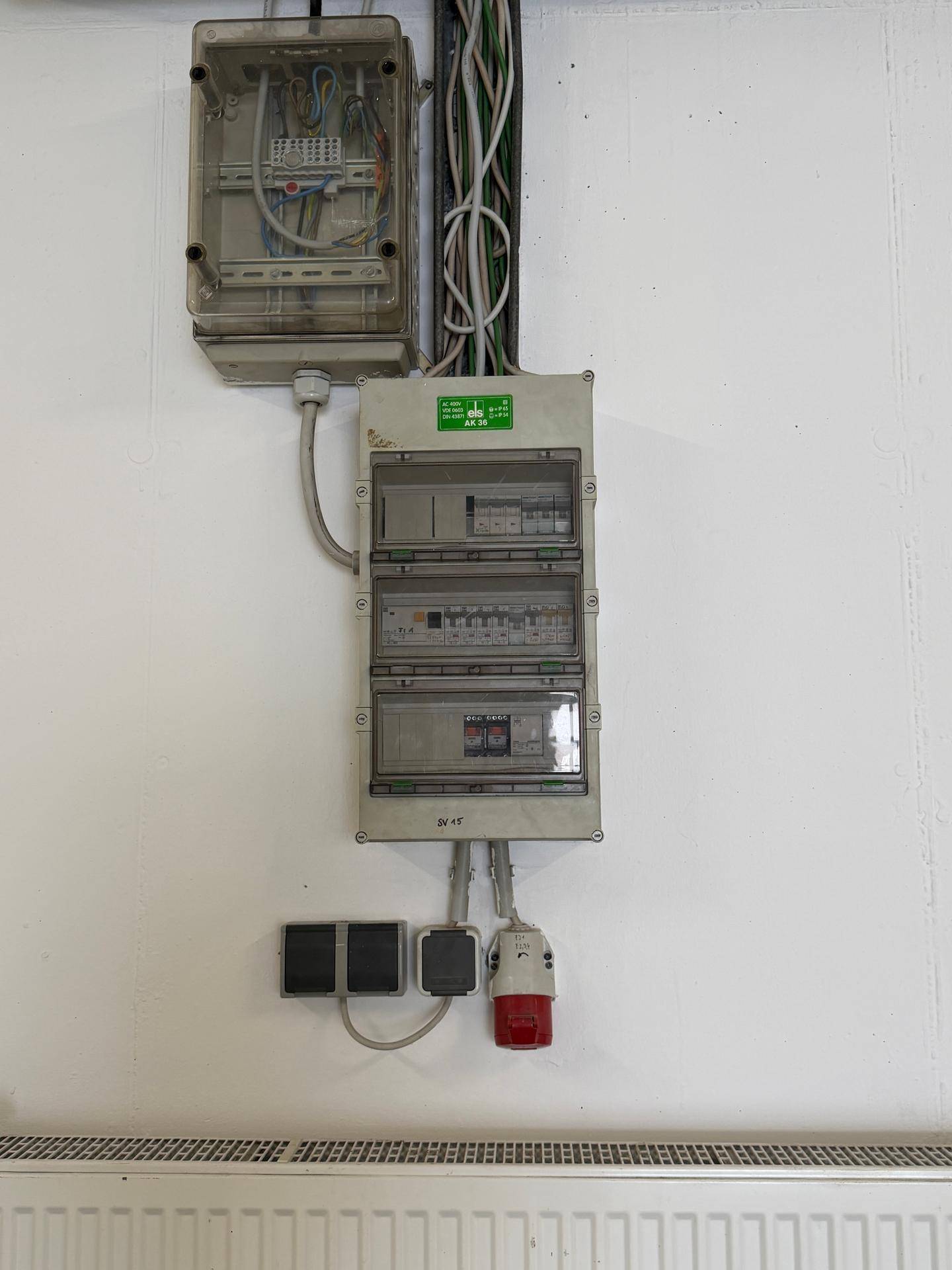 Elektrische Schaltkästen und Sicherungen an einer weißen Wand über einem Heizkörper.
