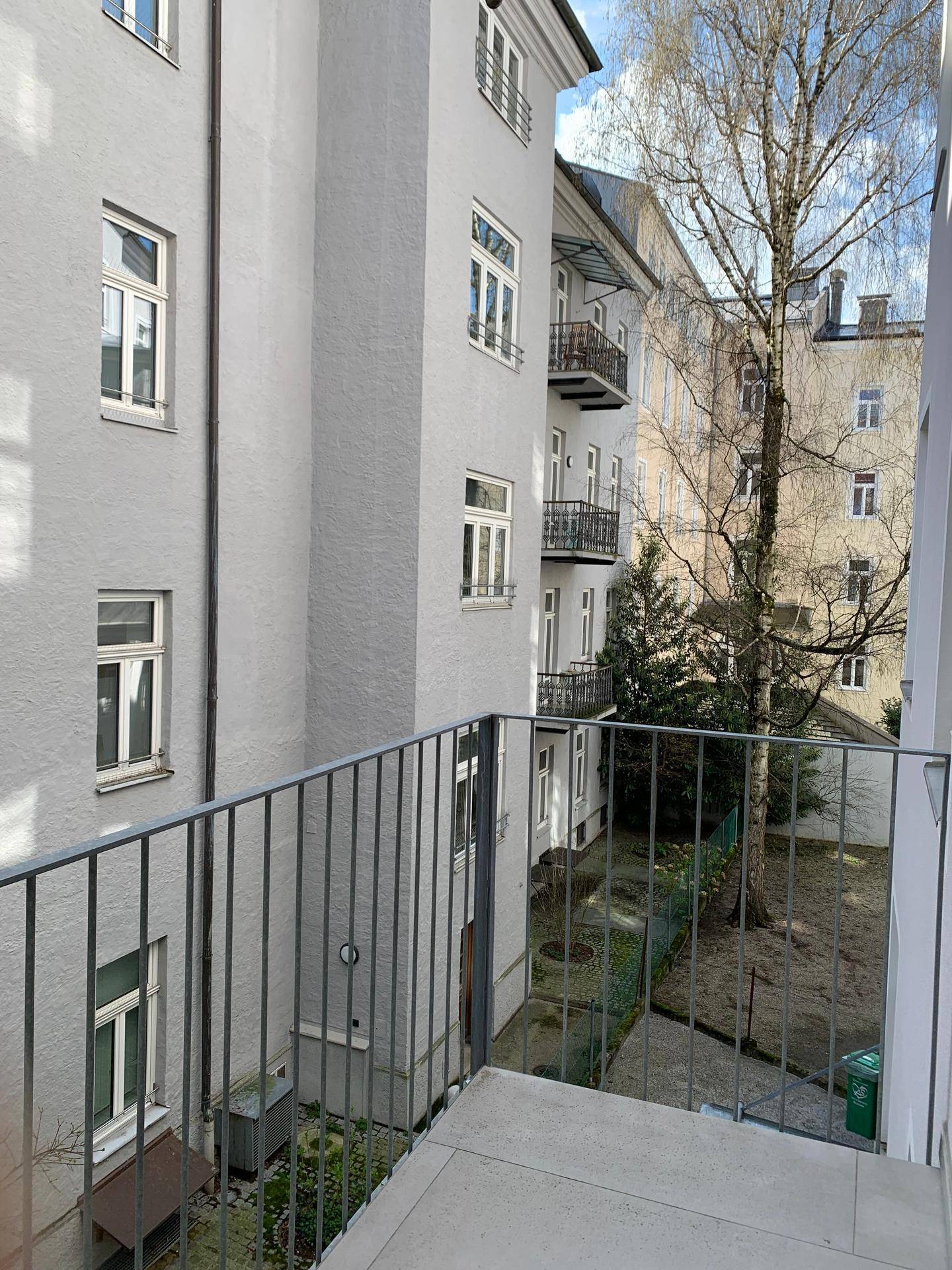 Balkon mit Metallgeländer und Blick auf den Innenhof mit Bäumen und Gebäuden.