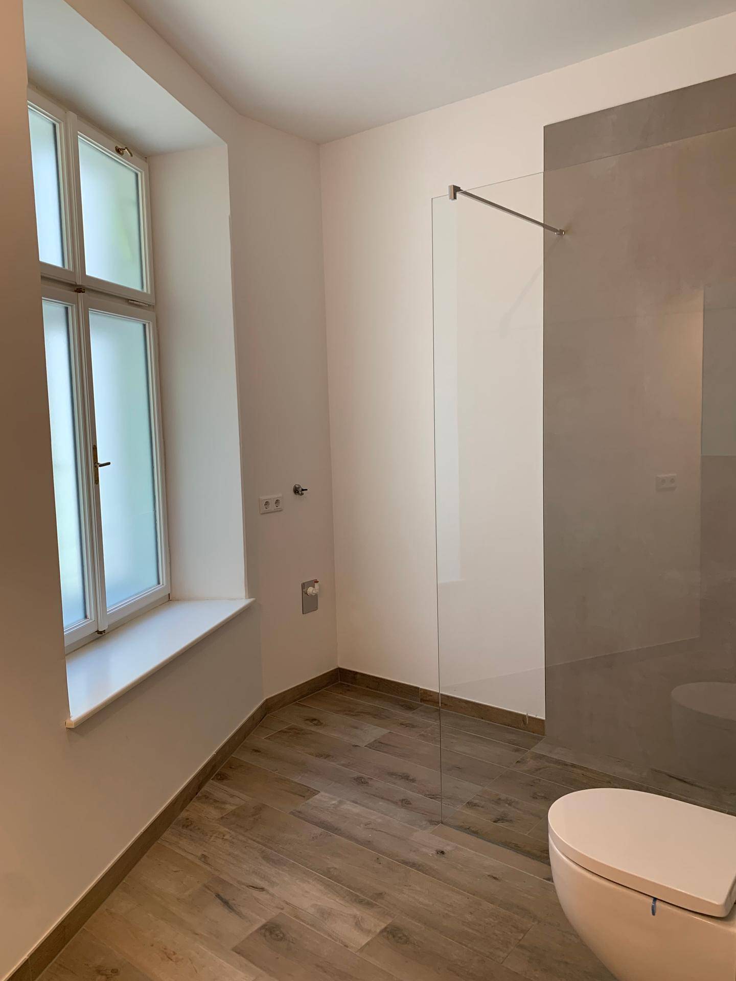 Geräumiges Badezimmer mit bodengleicher Dusche, wandhängendem WC und einem großen Fenster.