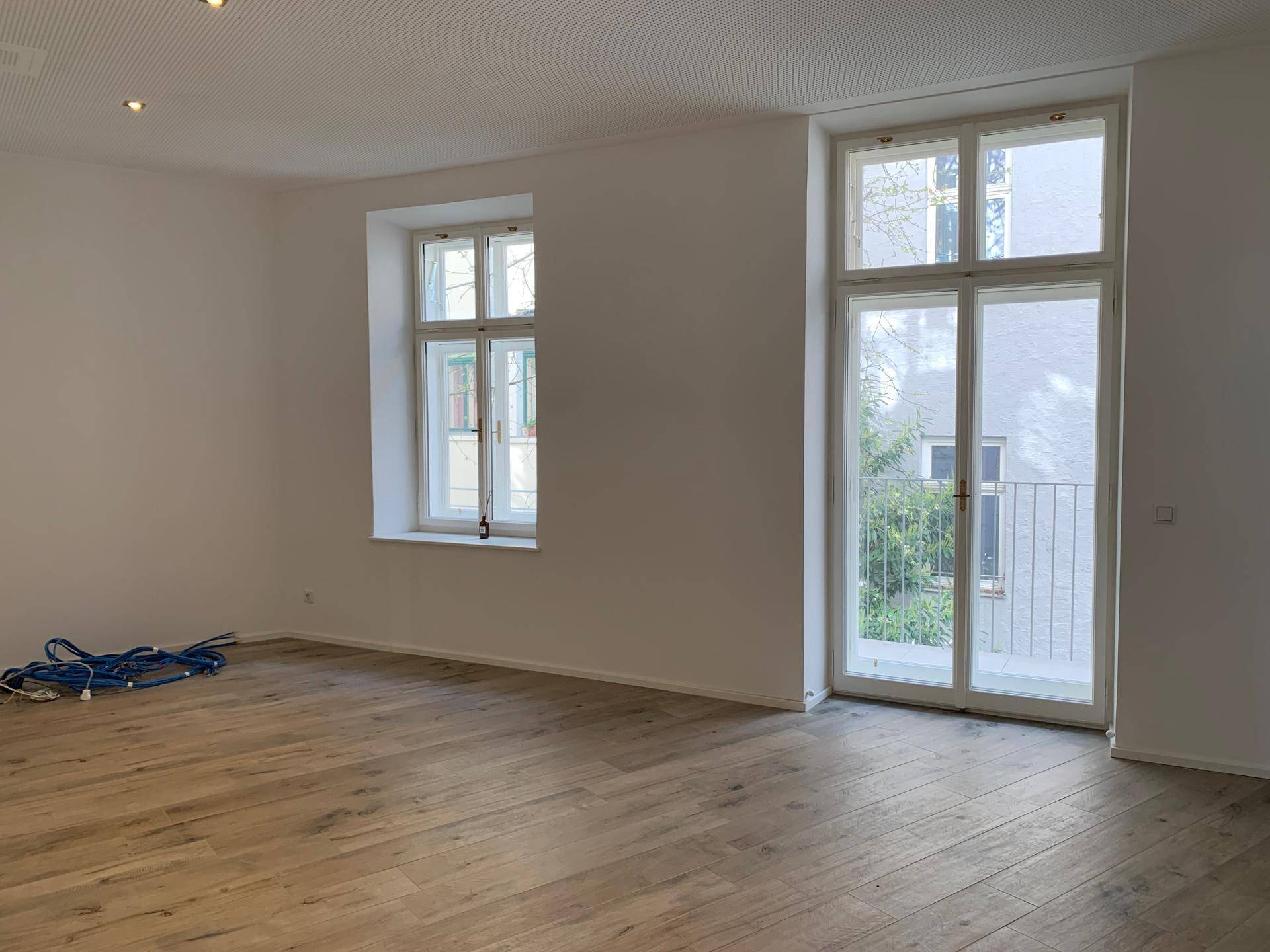 Heller Raum mit Holzboden und einer großen Fenstertür, die zu einem kleinen Balkon führt.