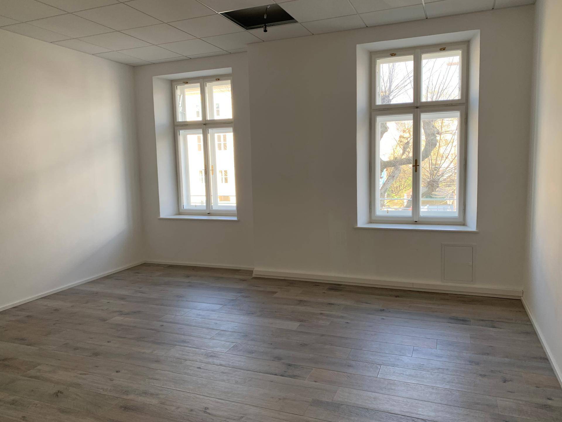 Heller, leerer Raum mit zwei Fenstern und modernem Holzboden, bereit zur Einrichtung.