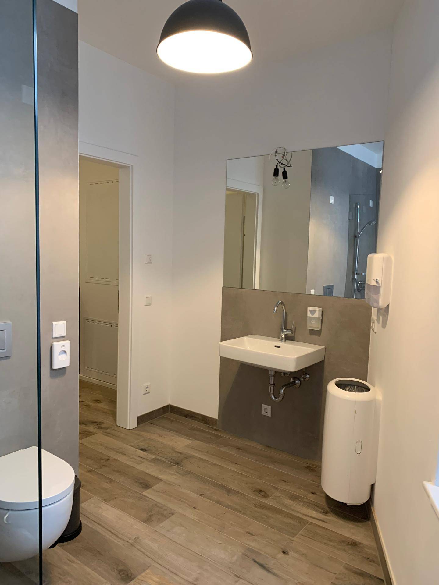 Modernes Badezimmer mit Holzbodenoptik, wandhängendem WC und einem eleganten Waschbecken.