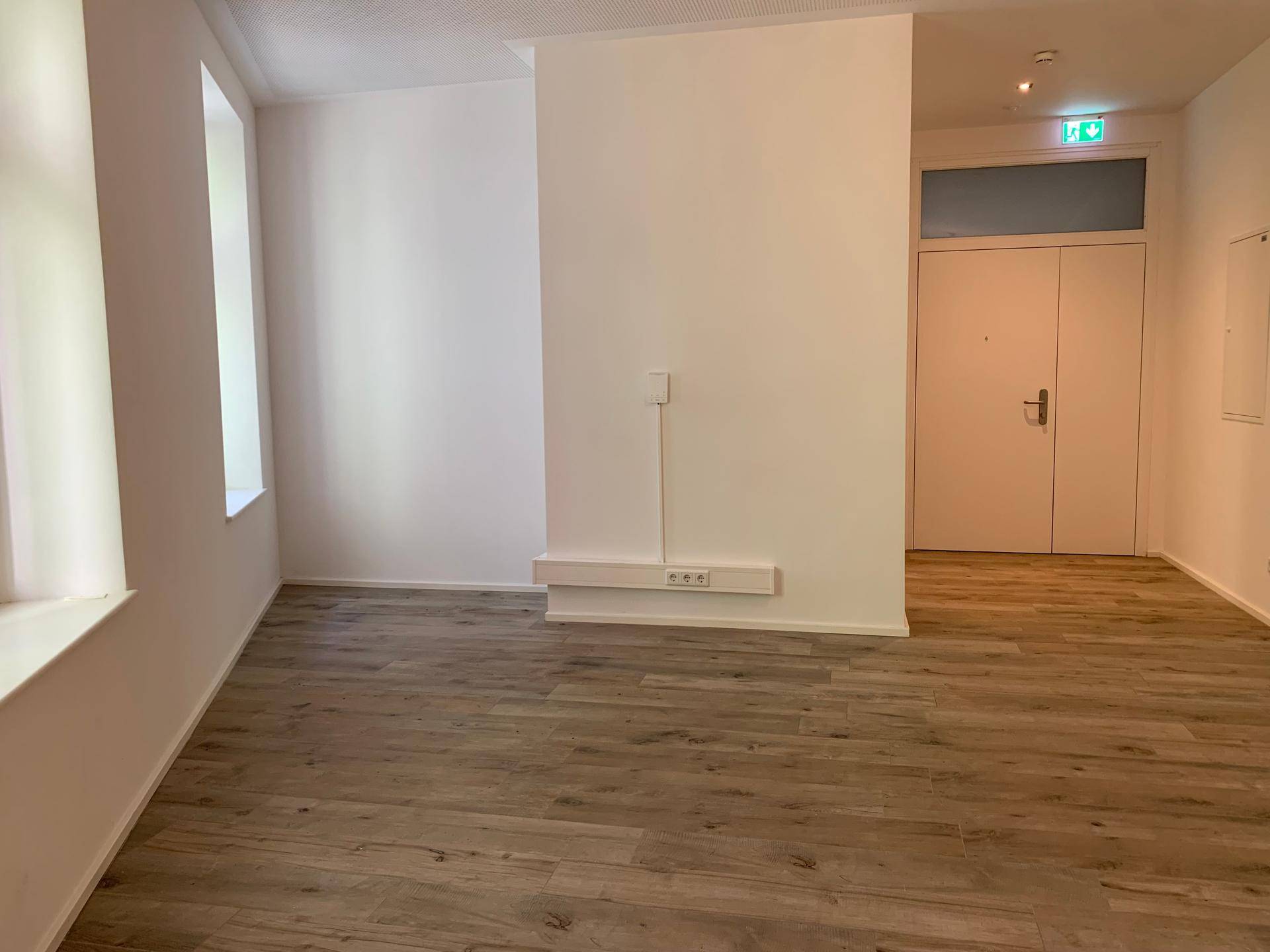 Heller, leerer Raum mit großen Fenstern und modernem Holzboden, ideal für ein Büro.
