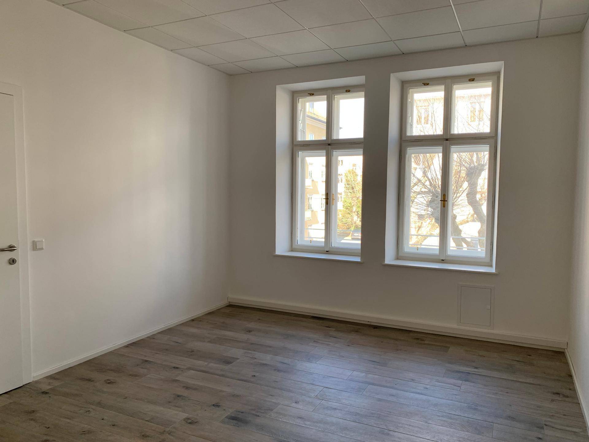 Geräumiger, heller Raum mit Holzboden und großen Fenstern, bereit zur individuellen Gestaltung.