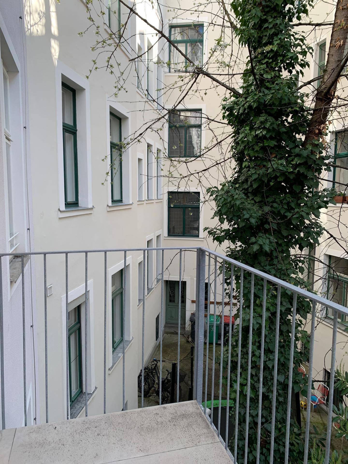 Balkon mit Blick auf den begrünten Innenhof und die umliegenden Gebäude.