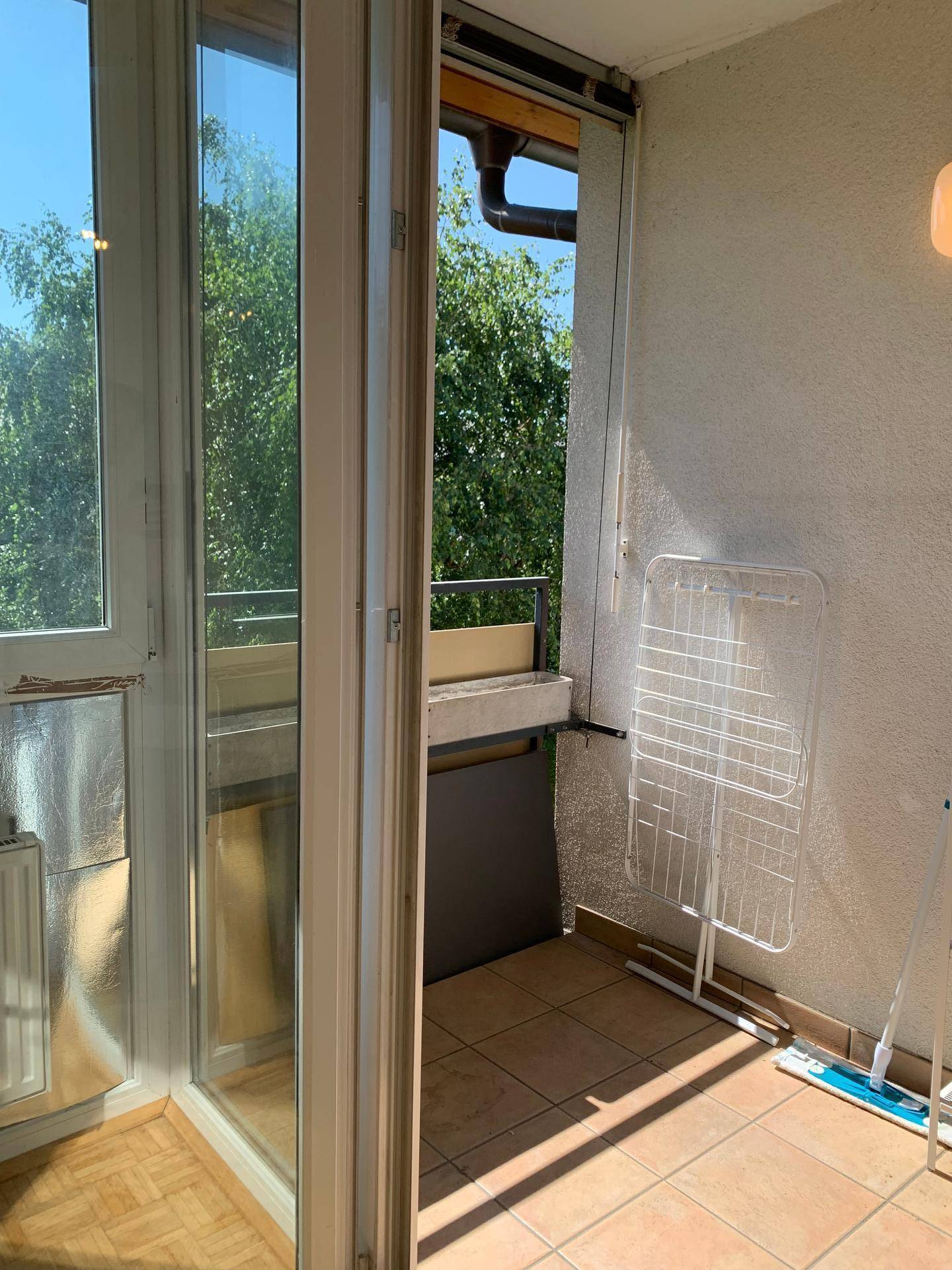 Sonniger Balkon mit Fliesenboden und Wäscheständer, umgeben von Bäumen.