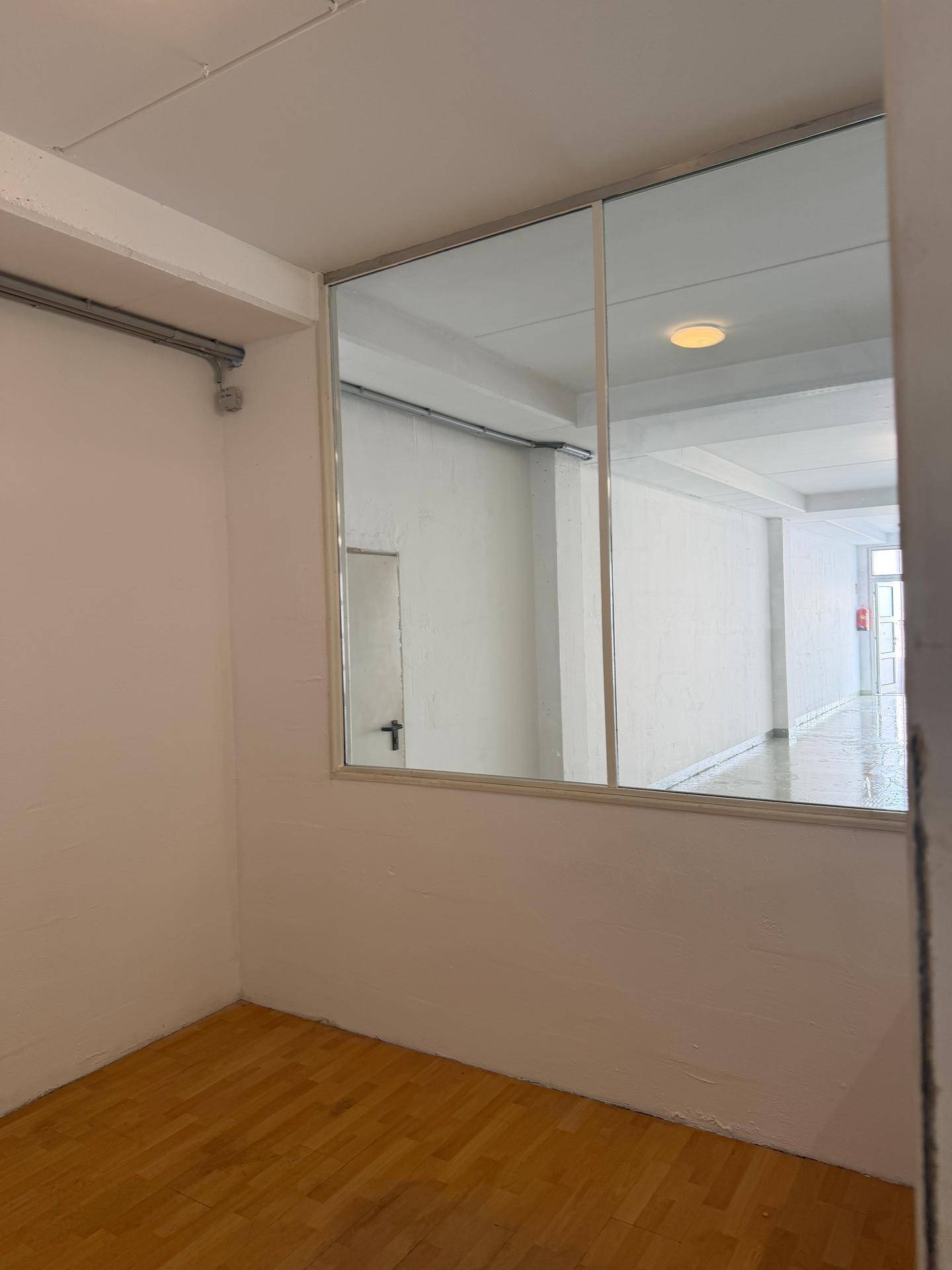 Büroraum mit Holzparkettboden und einer großen Fensterfront, die den Blick in den Hauptraum freigibt.