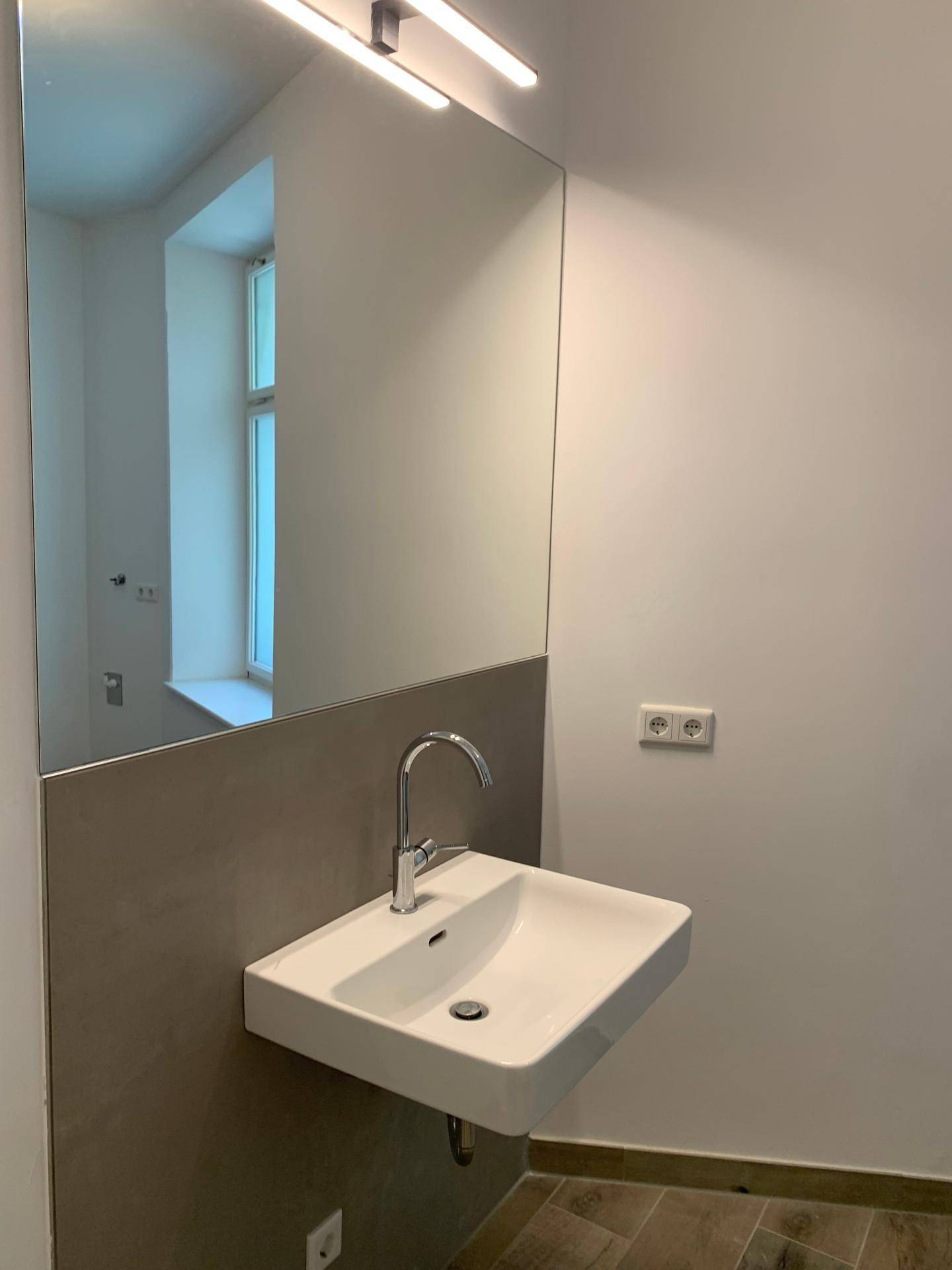Modernes Badezimmer mit wandhängendem Waschbecken, großem Spiegel und Fensterblick.