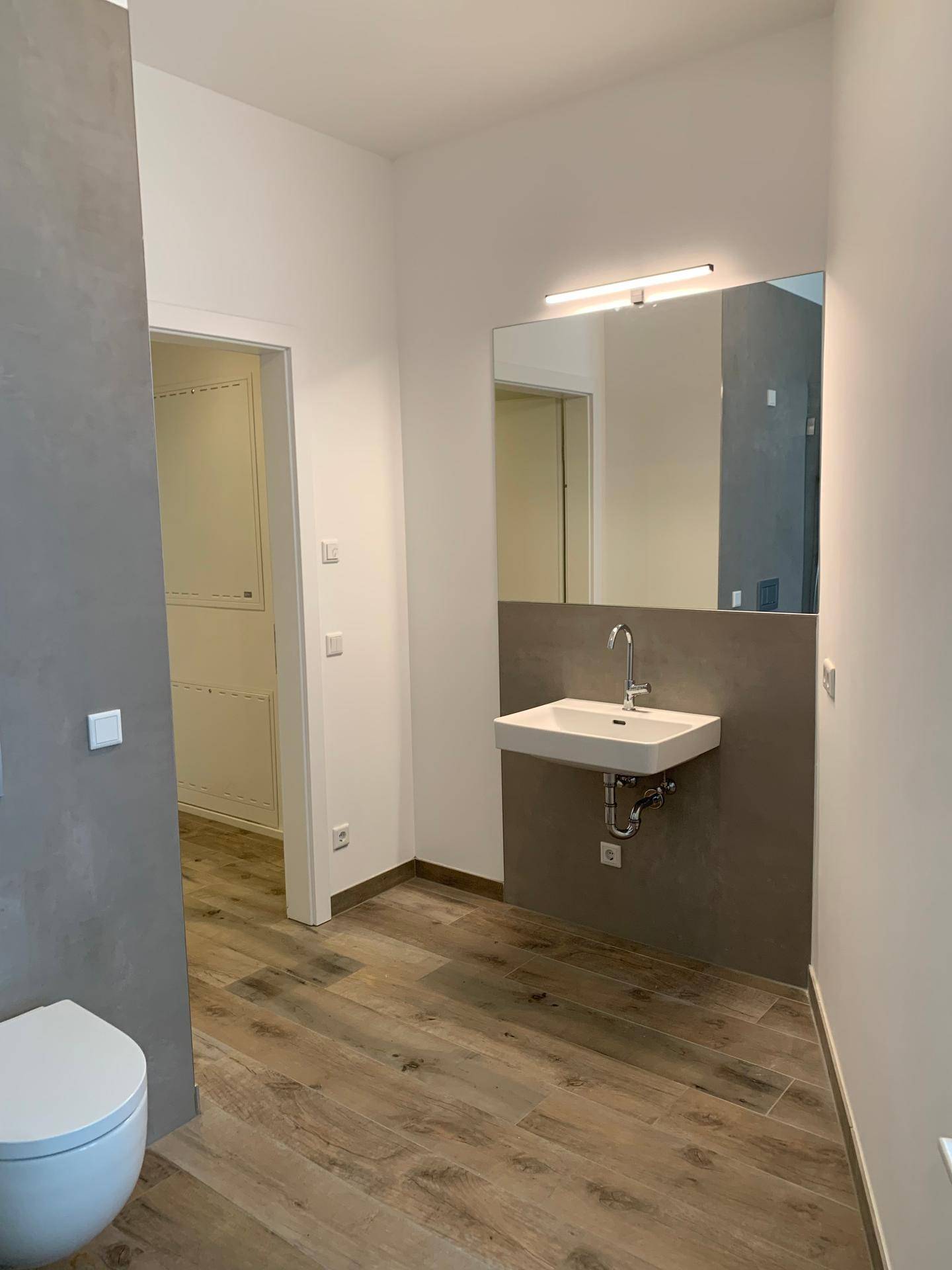 Helles Badezimmer mit Holzbodenoptik, wandhängendem WC und einem modernen Waschbecken.