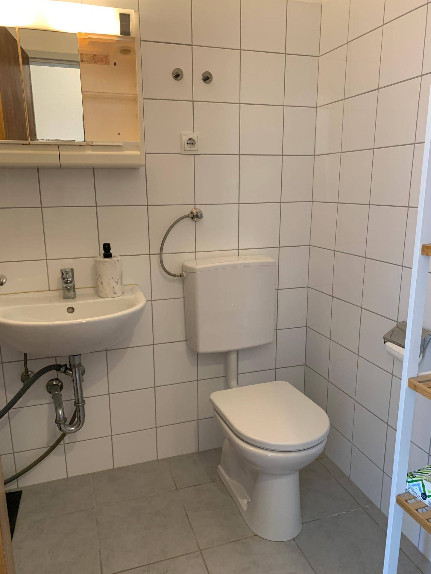 Kleines WC mit weißen Fliesen, Waschbecken und Spiegelschrank.