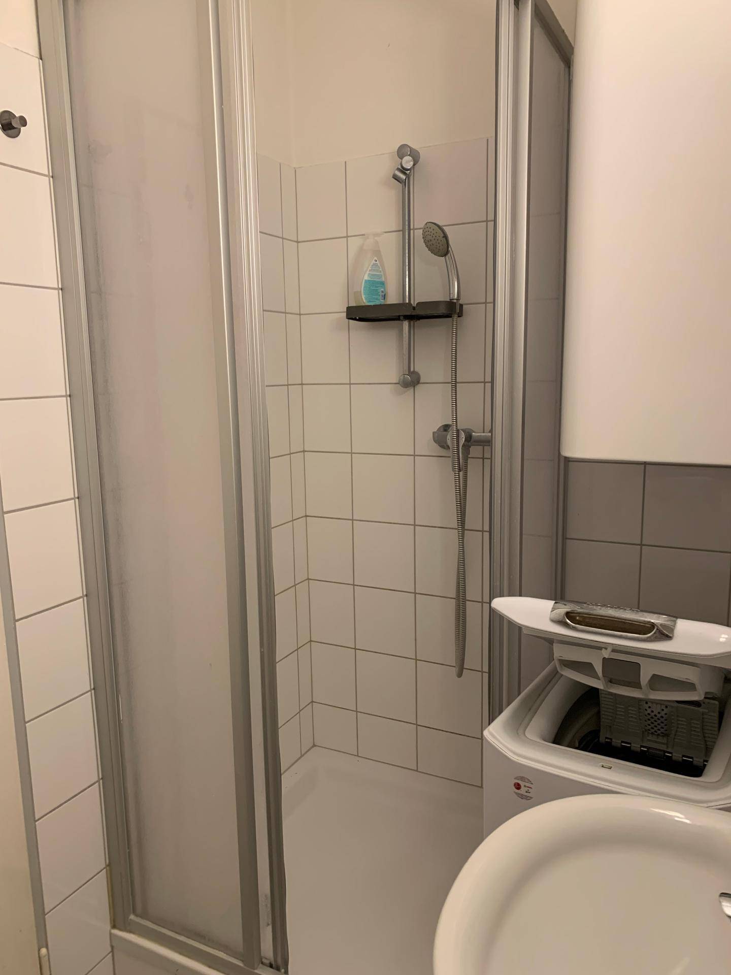 Badezimmer mit Duschkabine, Waschbecken und integrierter Waschmaschine.